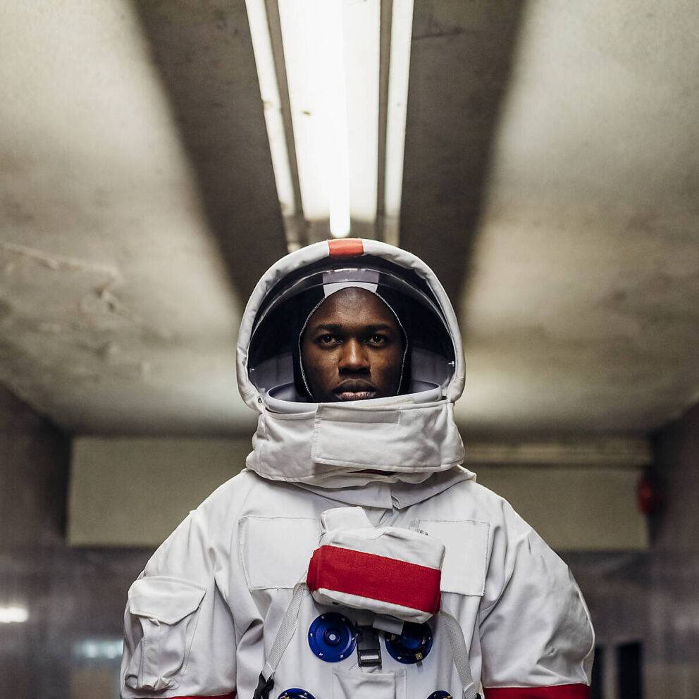 stock image, royalty-free, Young black astronaut wearing space suit in basement- Garibaldi District; Italy; Lombardy; Milan - freedom; ambition; new planets; exploration; surreal concept