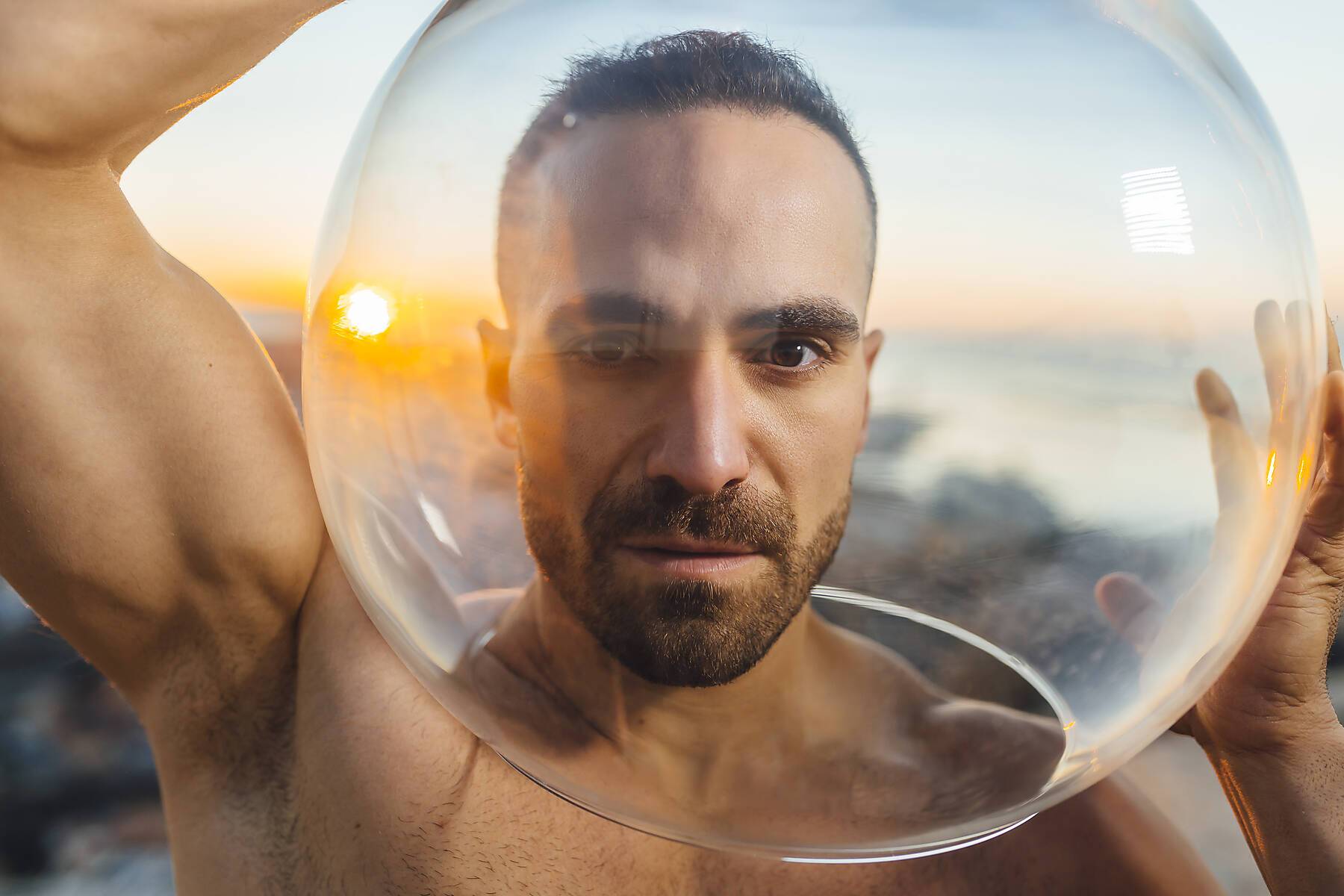 Man with hair stubble seen through glass bowl during sunrise