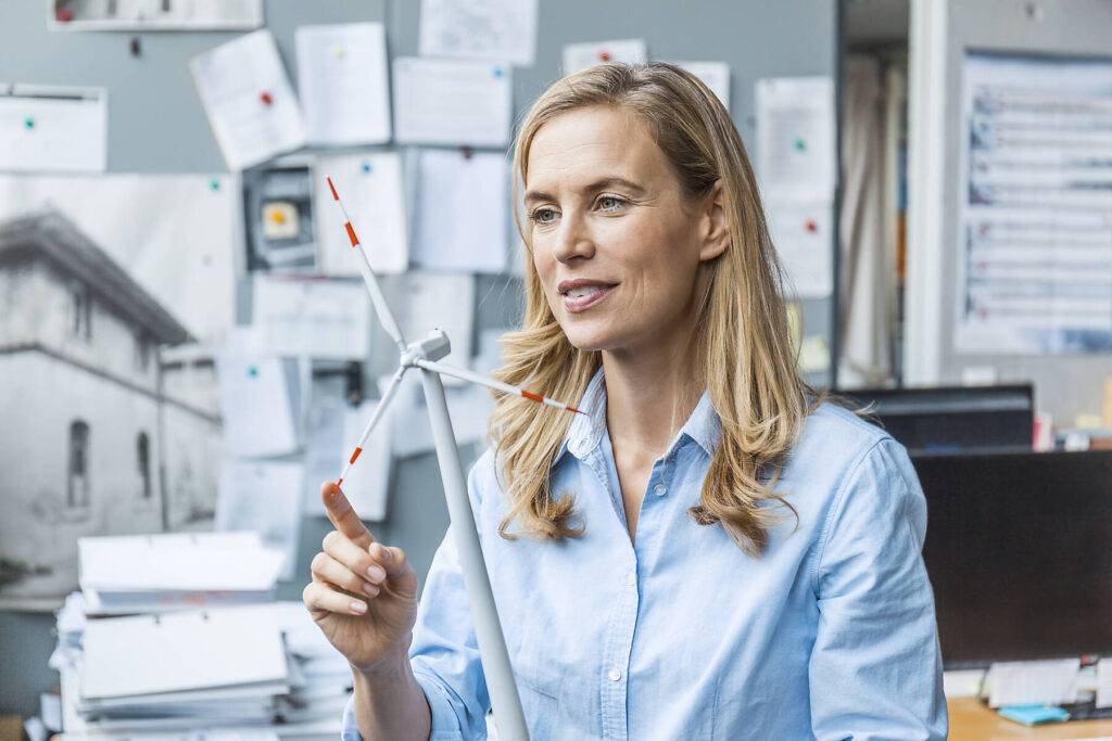 Confident woman in office holding wind turbine model