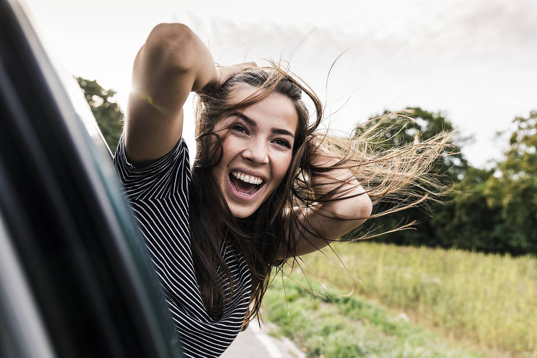 Carefree young woman leaning out of car window