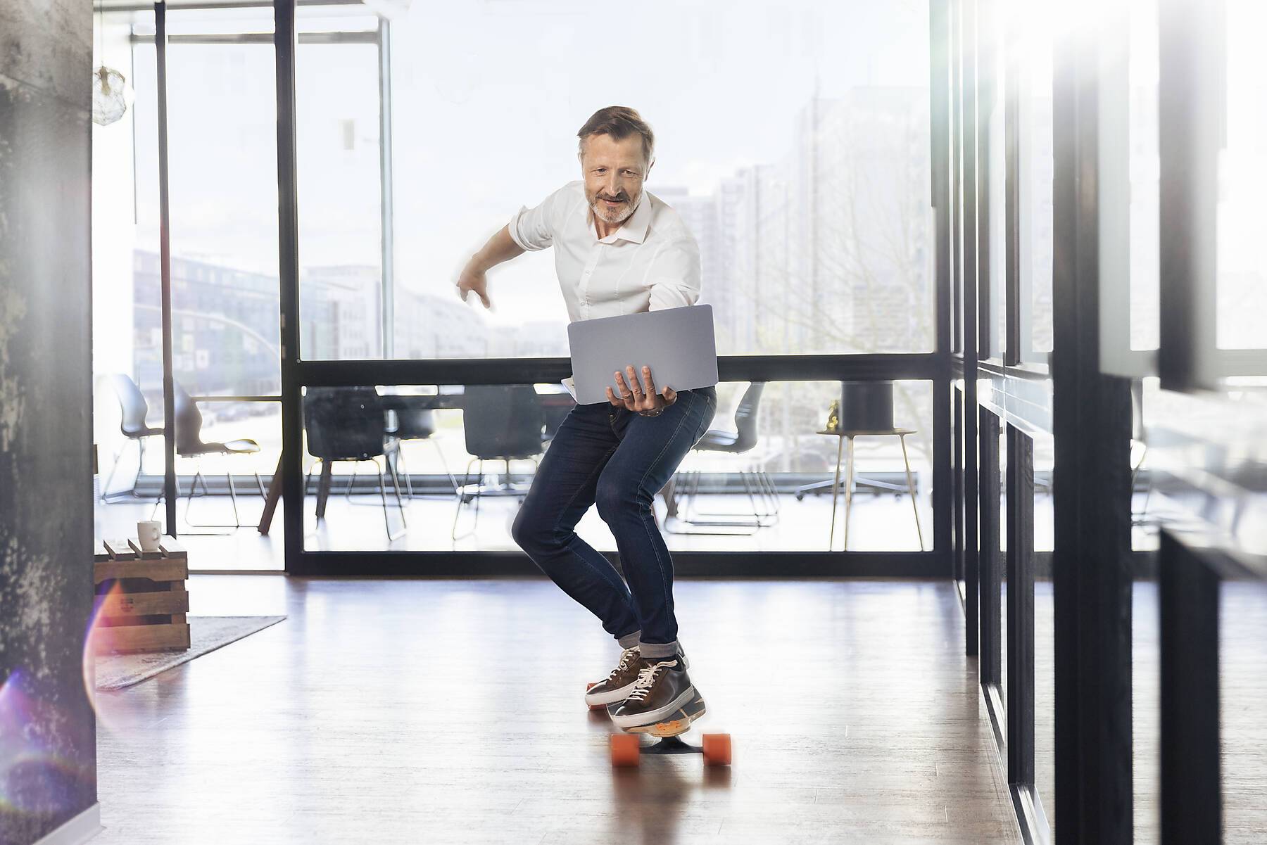 stock image, royalty-free, Mature businessman skateboarding looking at laptop in office