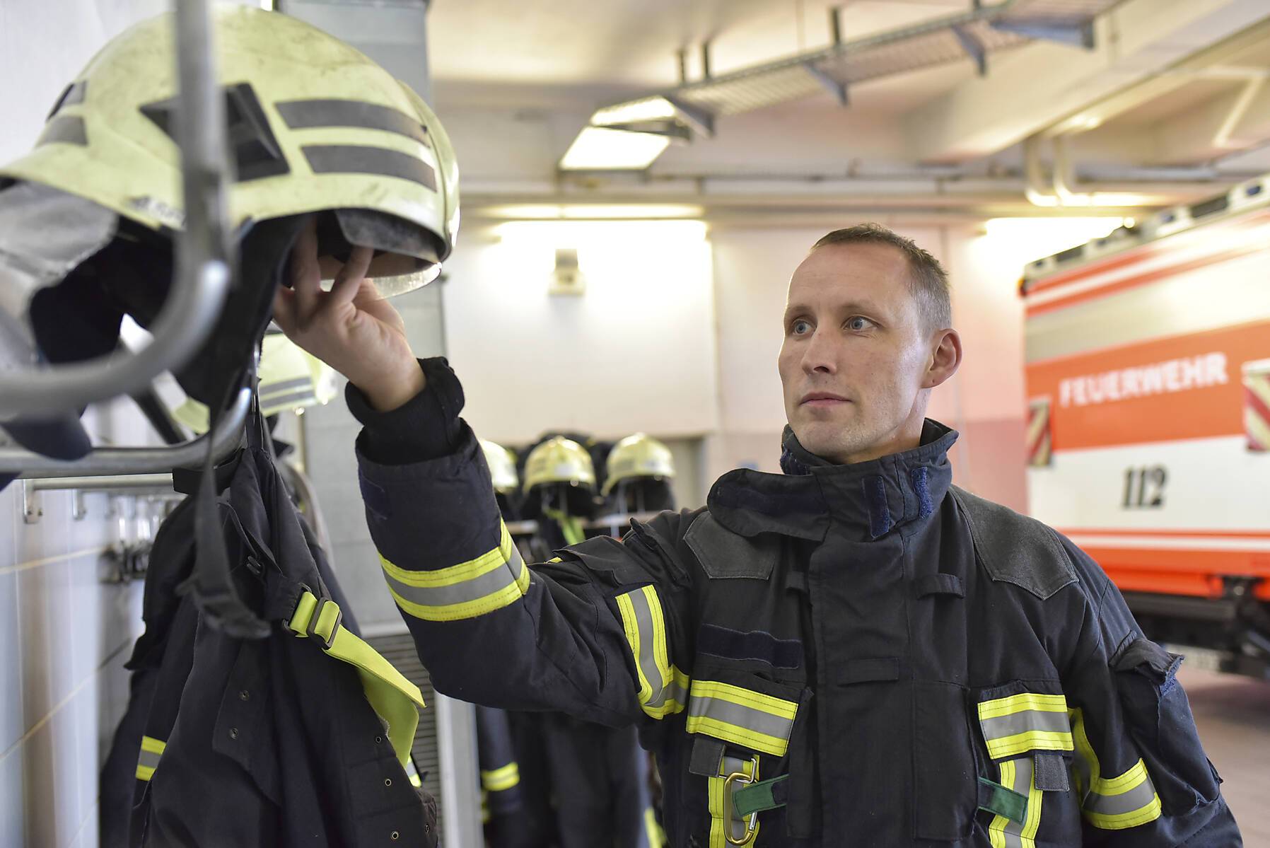 Firefighter taking helmet from rack in fire station