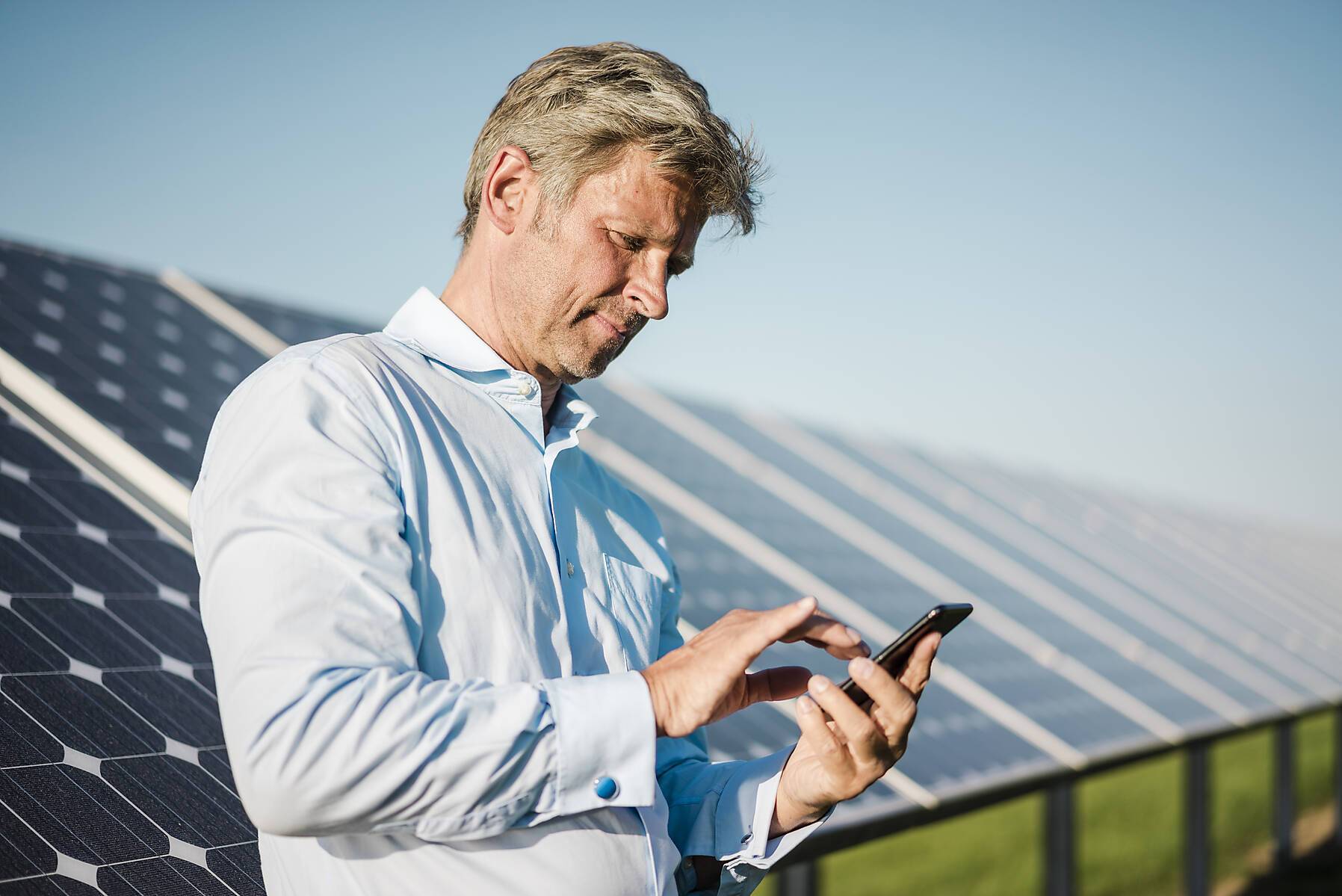 stockfoto, lizenzfrei, Geschäftsmann benutzt Smartphone im Solarpark