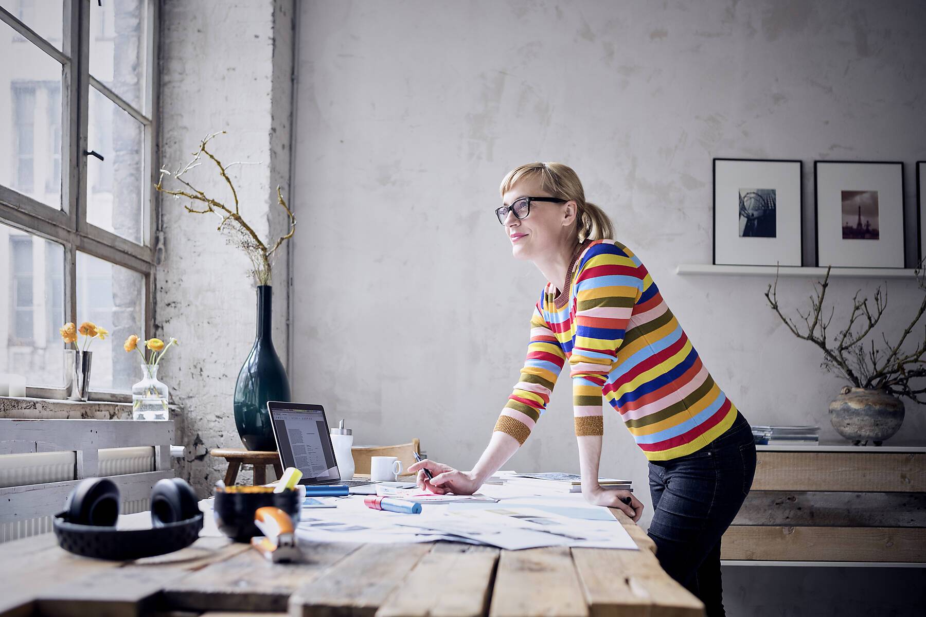 Stockfoto, lizenzfrei, Porträt einer lächelnden Frau, die in einem Loft am Schreibtisch steht und durch ein Fenster schaut