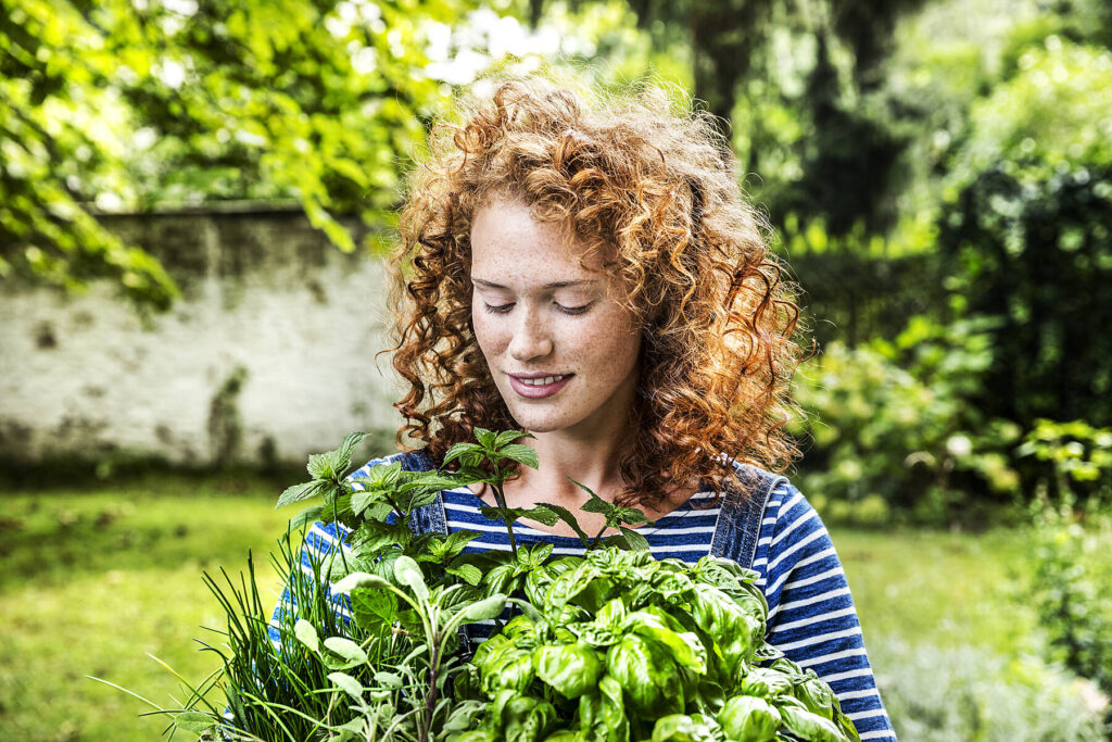 Stockfoto, lizenzfrei, Porträt einer jungen Frau mit frischen Kräutern im Garten