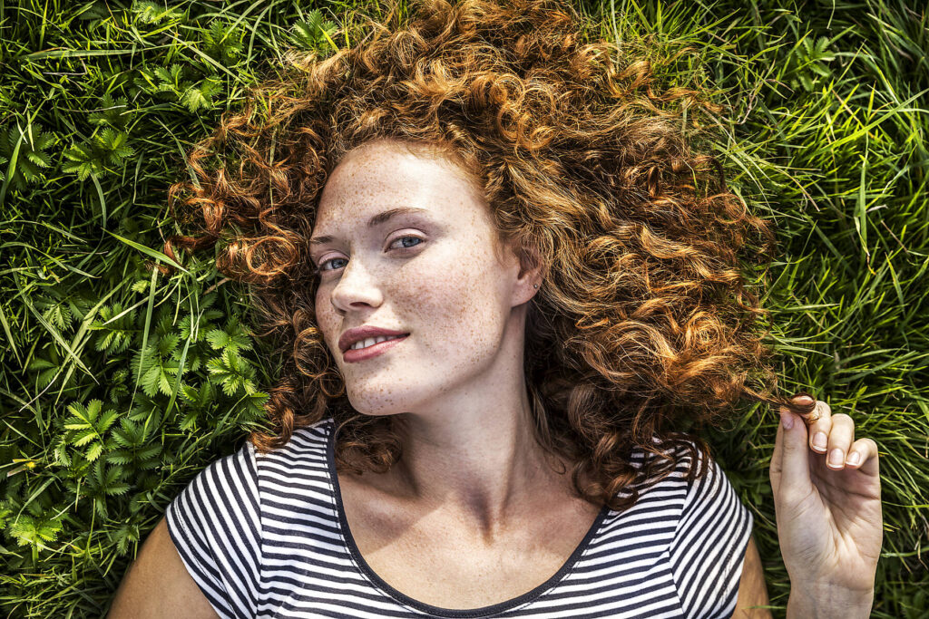 Stockfoto, lizenzfrei, Porträt einer lächelnden jungen Frau, die auf einer Wiese liegt