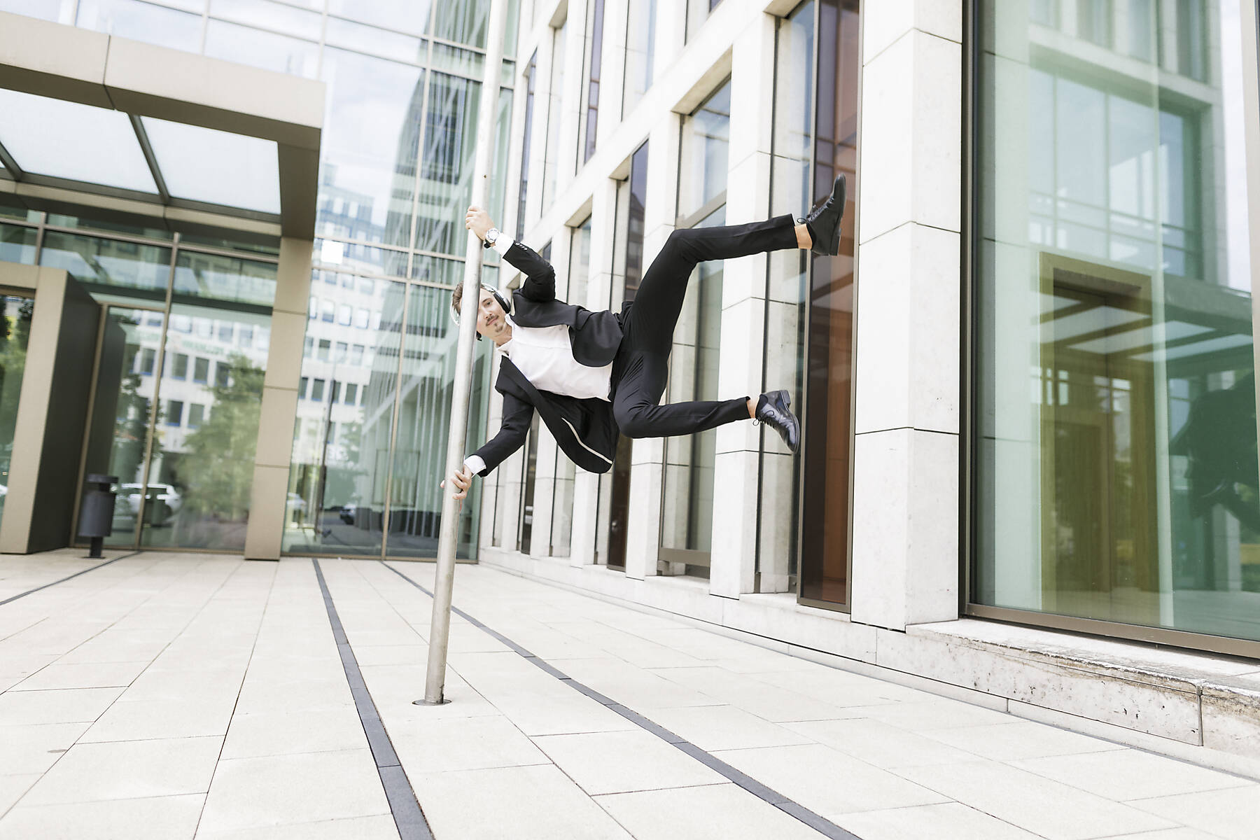 Stockfoto, lizenzfrei, Junger Geschäftsmann mit Kopfhörern springt am Laternenpfahl in der Stadt