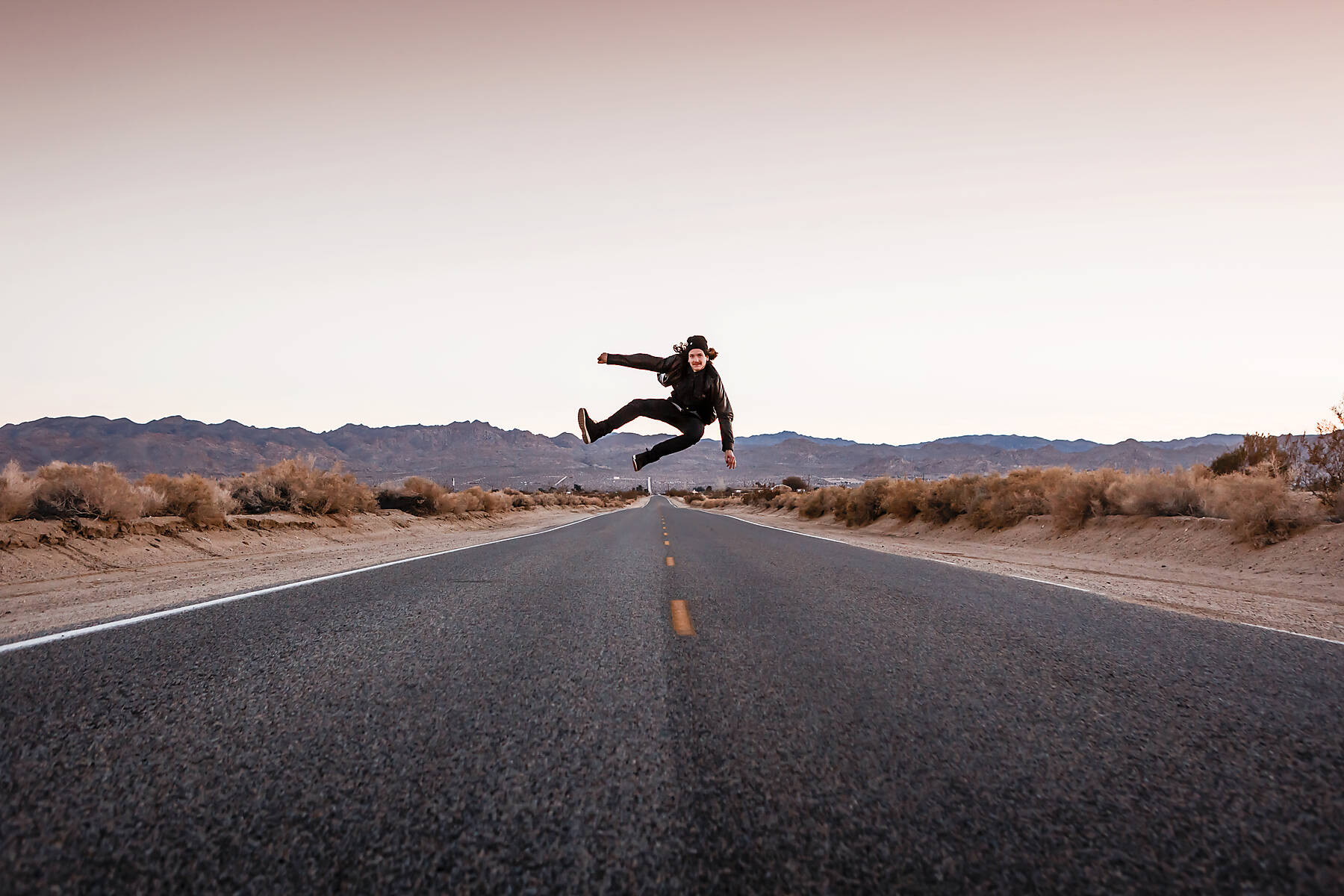 USA, California, Joshua Tree, young man jumping on a road
