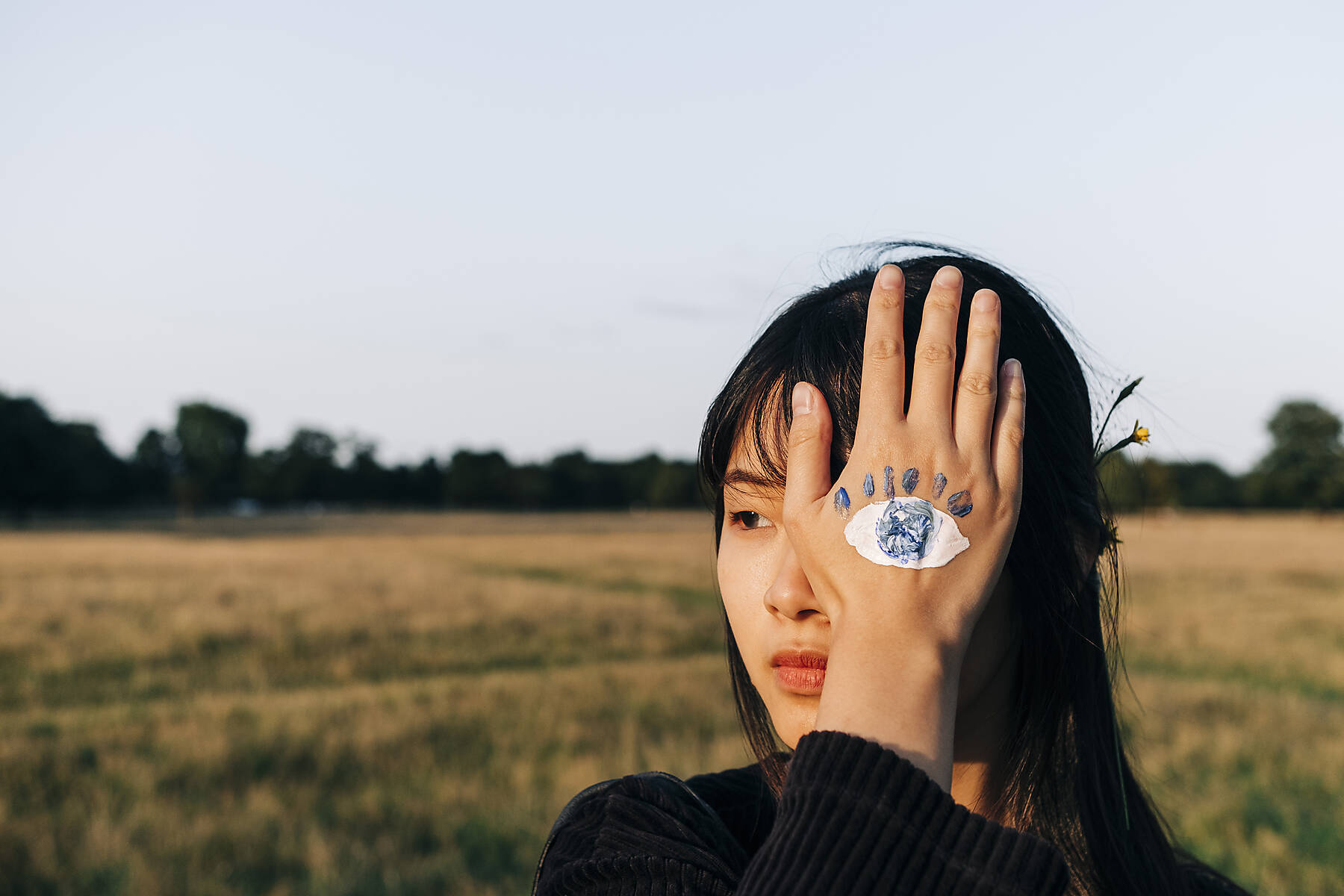 Stockfoto lizenzfrei, Junge Frau mit Farbe auf der Hand, die das Auge im Park verdeckt