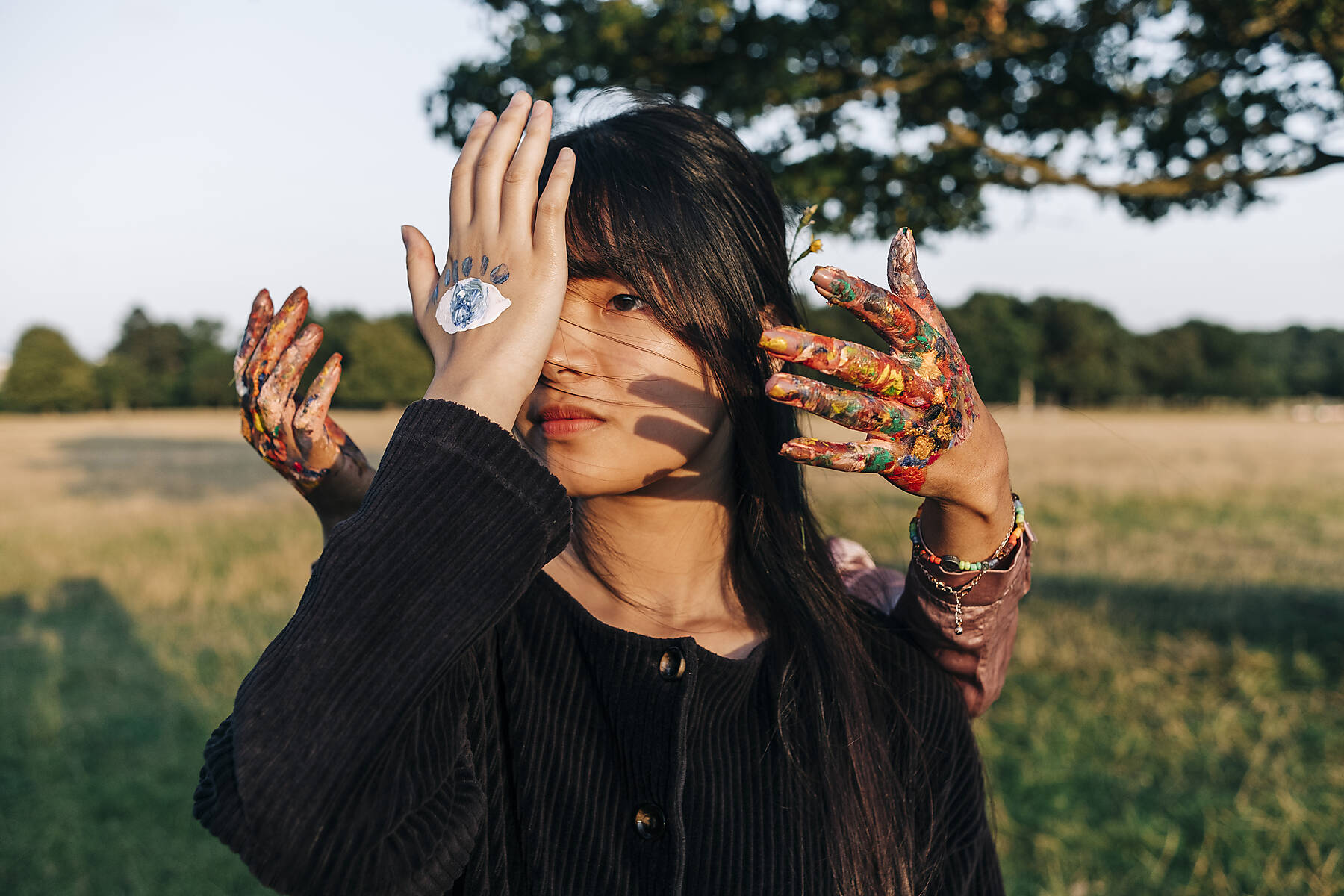 Stockfoto, lizenzfrei, Junge Frau mit Farbe auf der Hand, die das Auge im Park verdeckt
