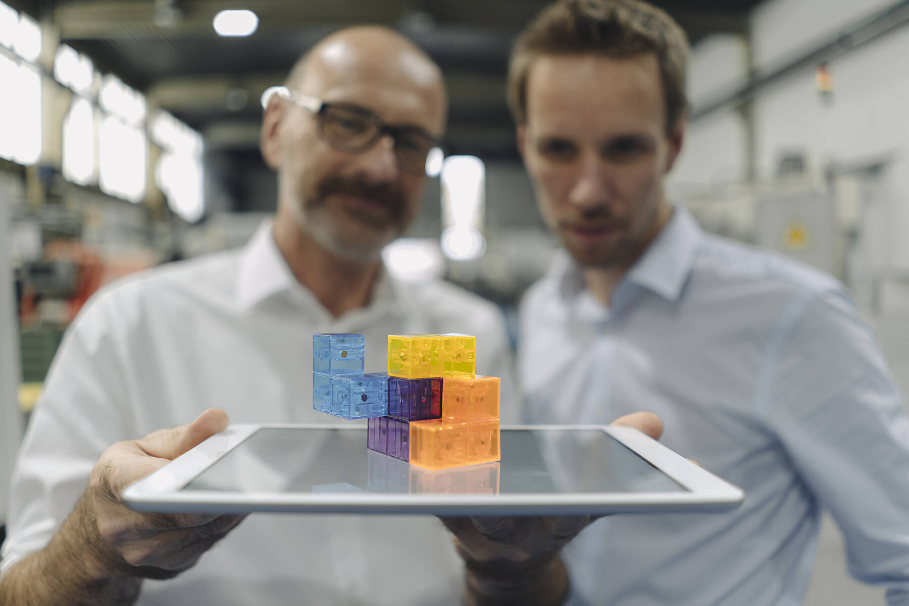 Two men examining workpiece on tablet in a factory, stock image, royalty-free