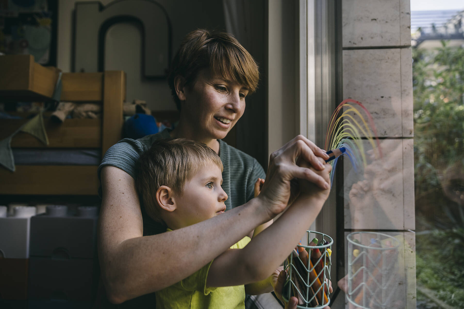 Stockfoto, lizenzfrei, Mutter und kleiner Sohn malen zu Hause Regenbogen am Fenster