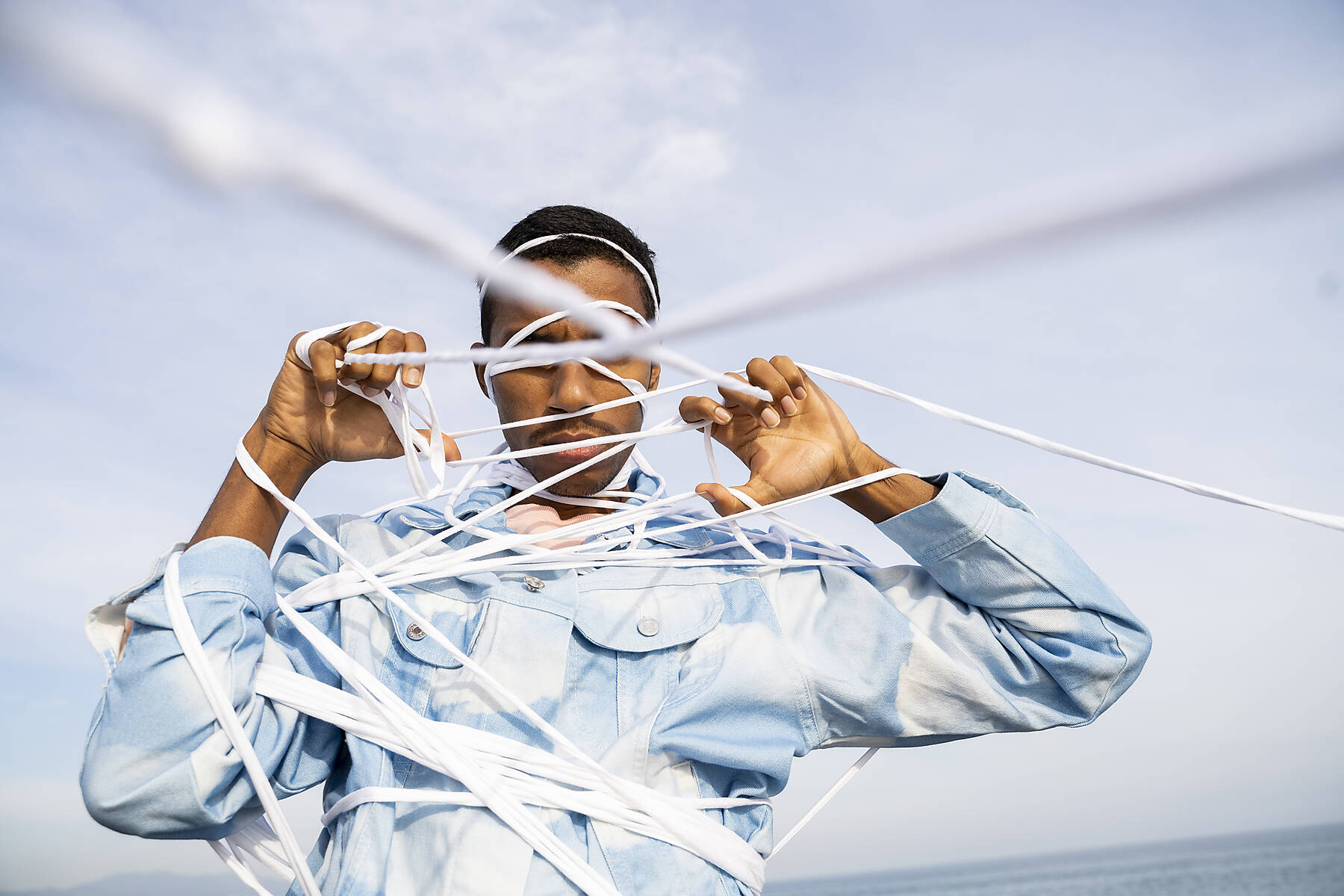 Young man struggling to escape from rope while standing against sky, stock image, royalty-free, Freedom, liberation, burden, setting free, free, scape, tangled, trapped, go away