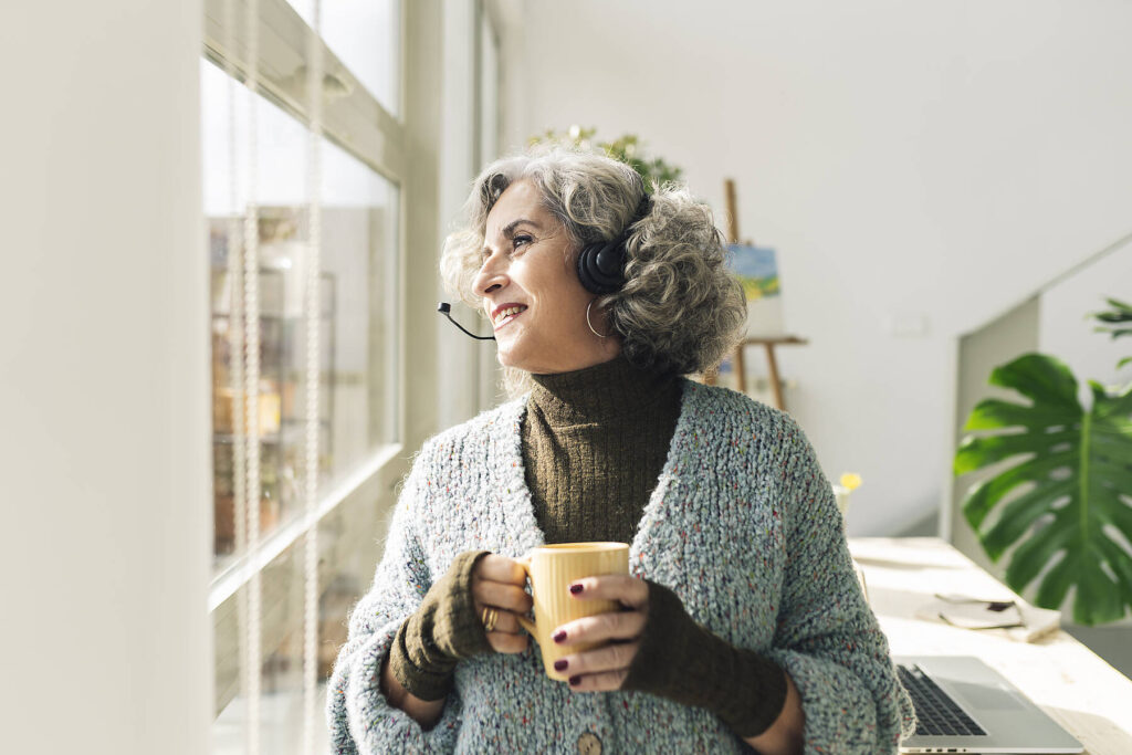 stockfoto, lizenzfrei, Lächelnde Geschäftsfrau, die aus dem Fenster schaut und eine Tasse im Büro zu Hause hält