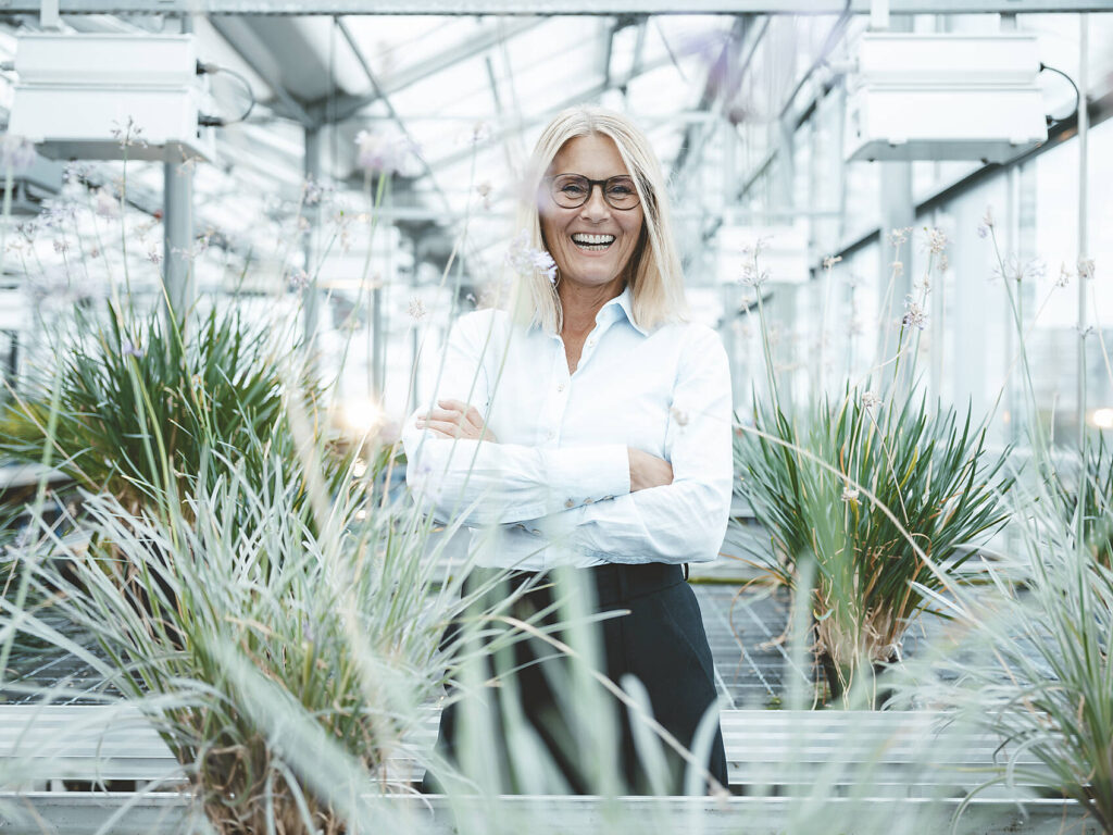 Stockfoto, lizenzfrei, Fröhliche Wissenschaftlerin inmitten von Pflanzen im Gewächshaus