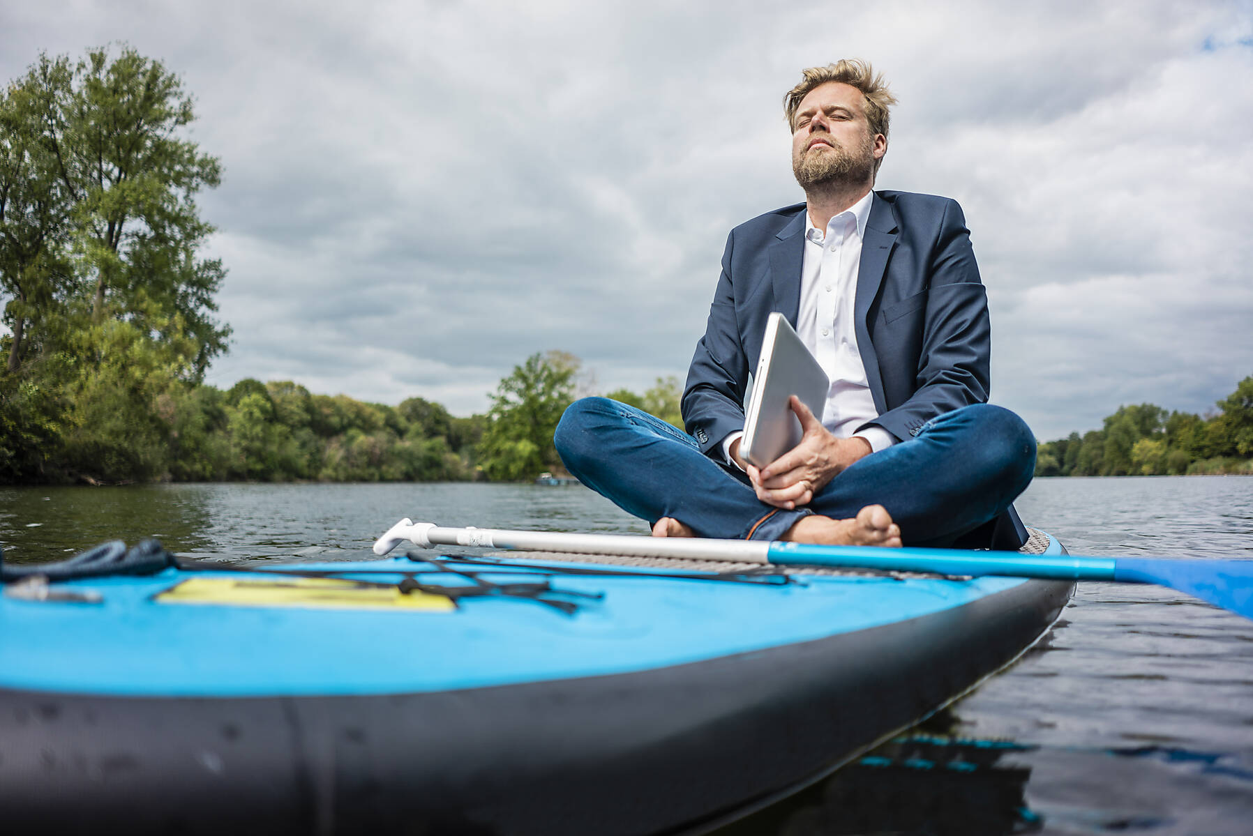 stock image, royalty-free, Businessman with laptop sitting on SUP board on a lake, escapism, reality