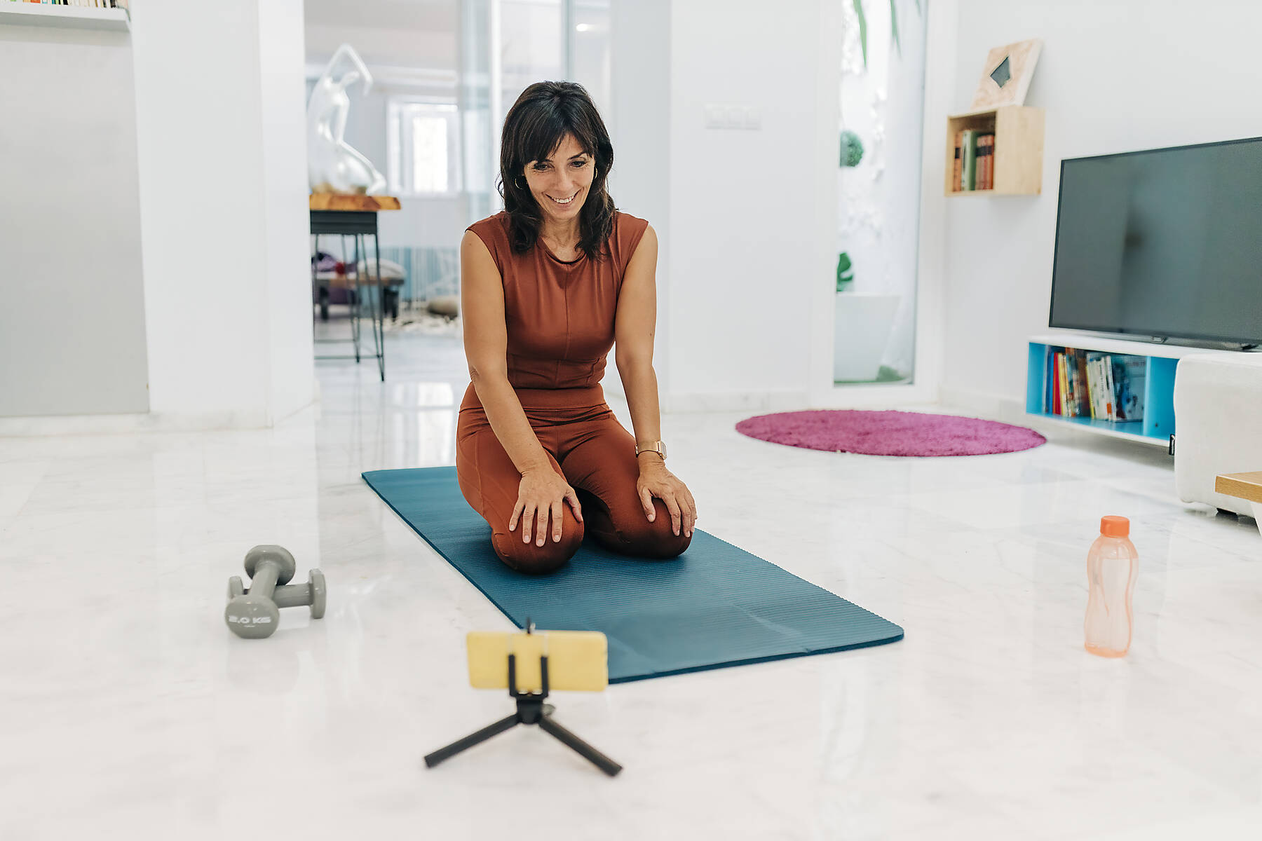 stock image, royalty-free, Smiling woman vlogging through smart phone while kneeling on exercise mat in living room