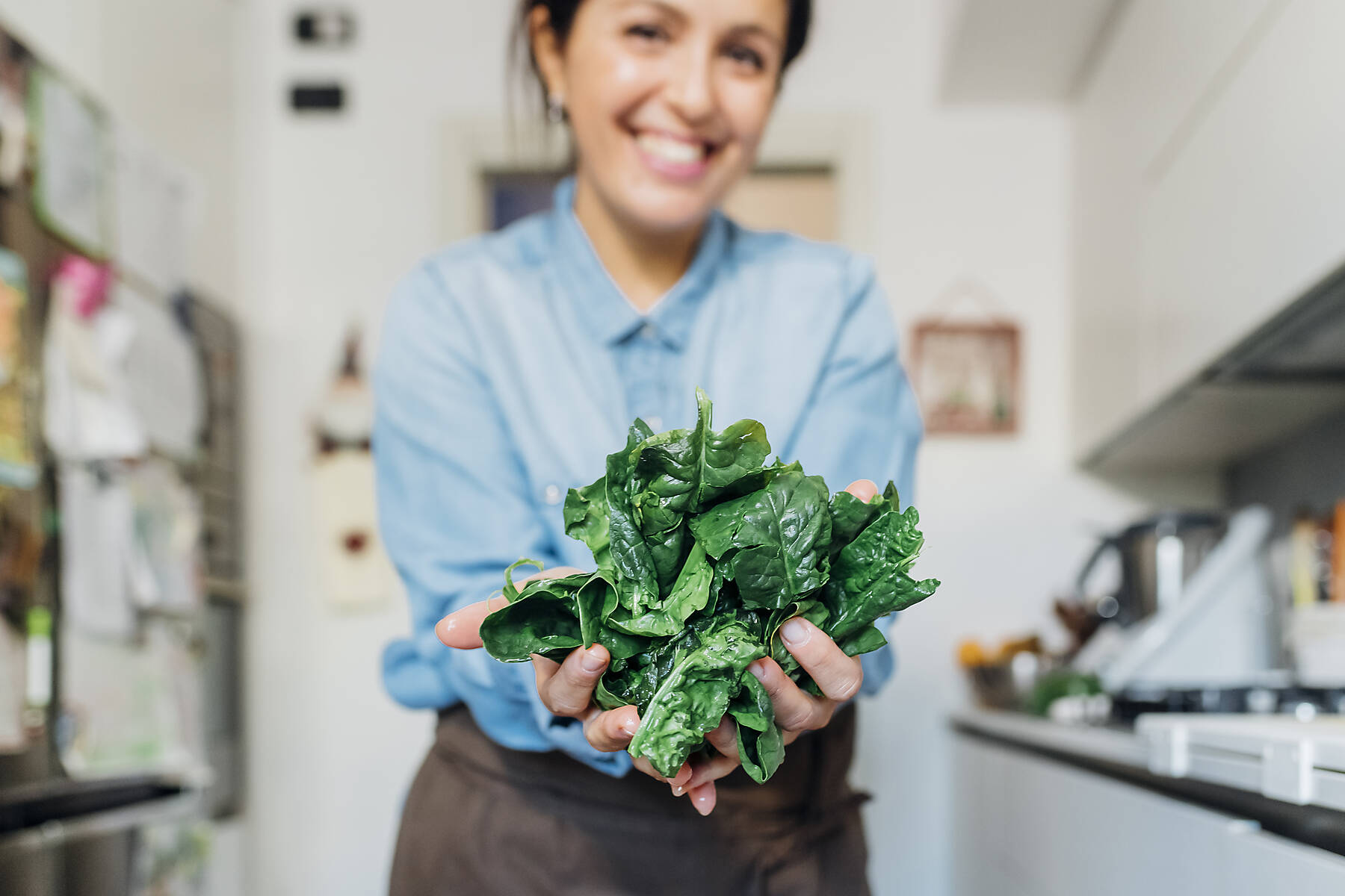 Stockfoto, lizenzfrei, Lächelnde Frau mit frischen Spinatblättern in der Küche zu Hause
