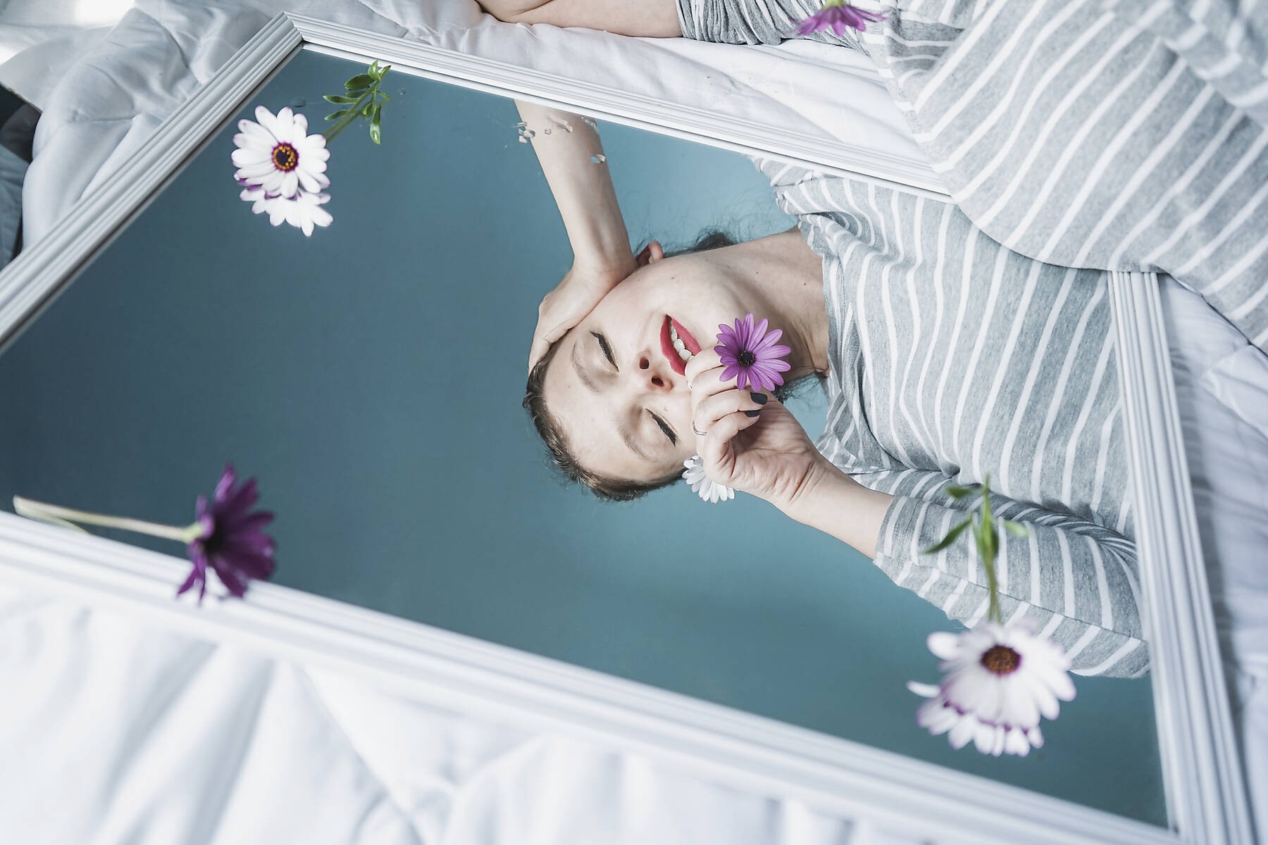 stock image, royalty-free, Young and pretty woman reflected in a mirror and surrouded by flowers in a blue room