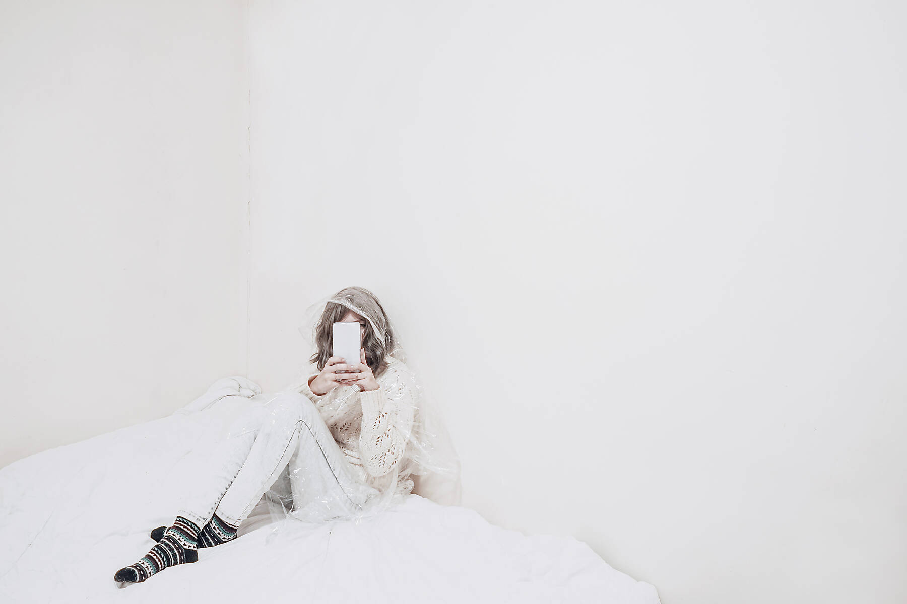 stock image, royalty-free, Woman using smart phone sitting on duvet in confined place