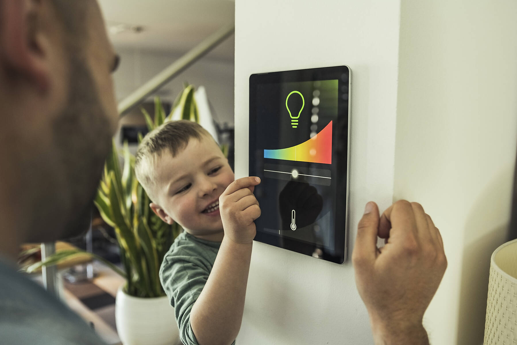Stockfoto, lizenzfrei, Lächelnder Junge, der mit seinem Vater im Smart Home die Lichter auf einem digitalen Tablet einstellt