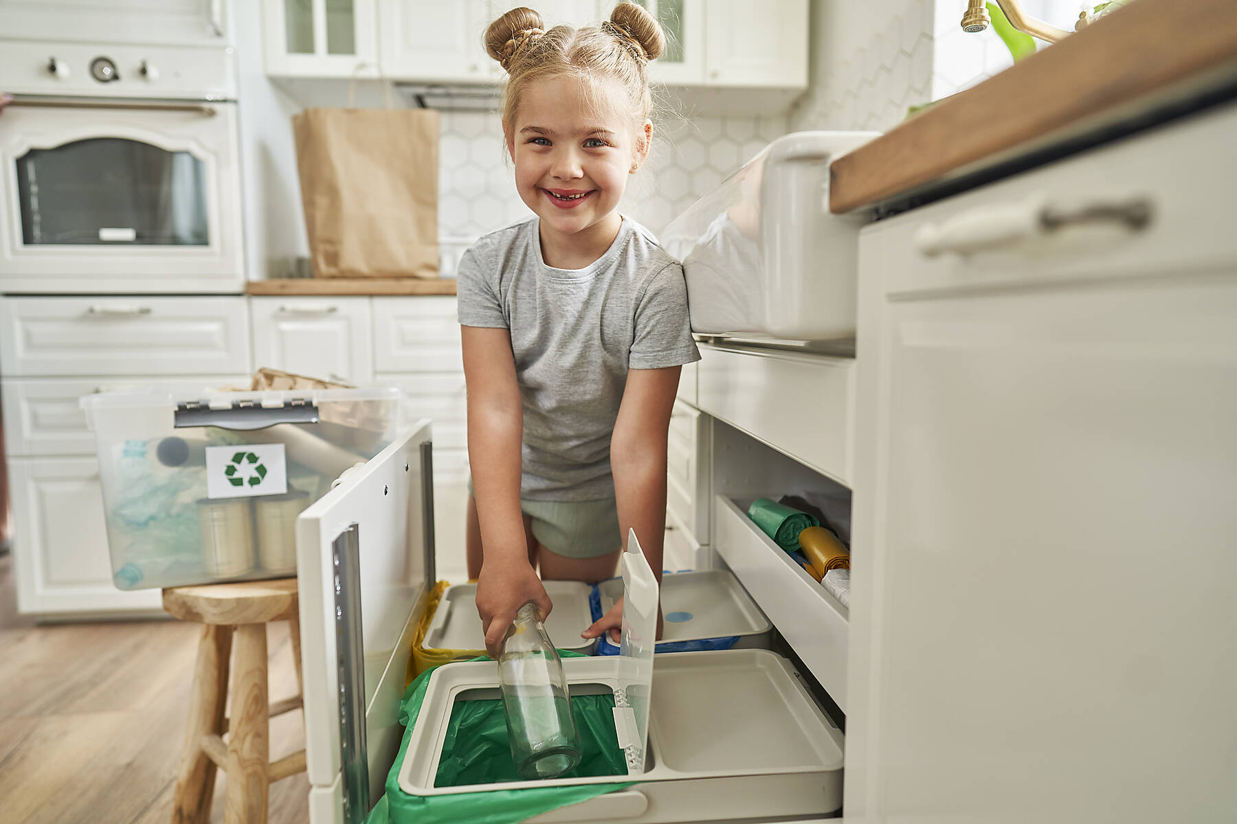 stock image, royalty-free, Smiling girl throwing glass bottle in garbage bin at home