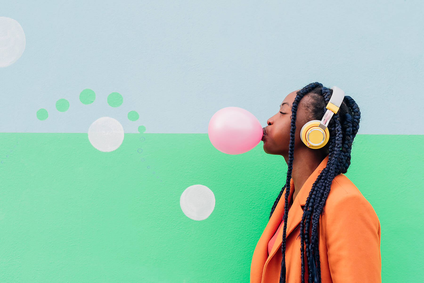 Italy, Milan, Stylish woman with headphones blowing gum in front of a colorful wall