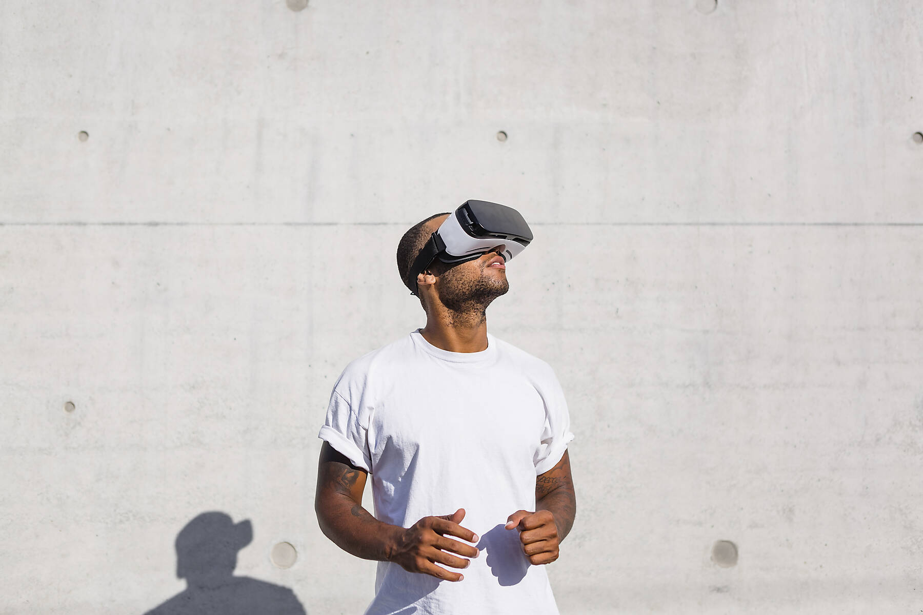 Man in white t-shirt in front of white wall with virtual reality glasses, stock photo, royalty free