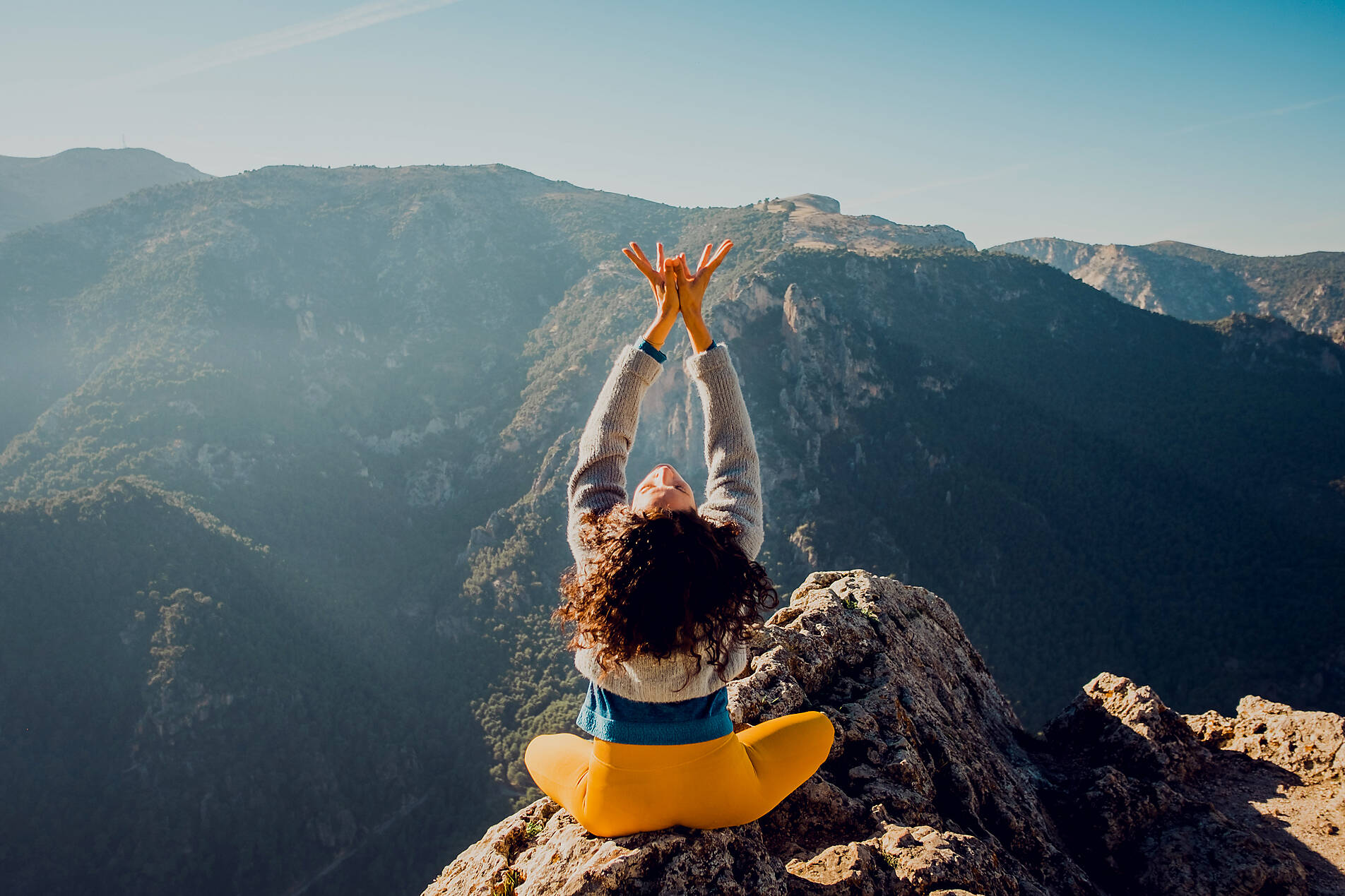 Stockfoto, lizenzfrei, Rückenansicht eines anonymen weiblichen Reisenden, der auf einem Felsen im Hochland sitzt und Yoga in Padmasana macht