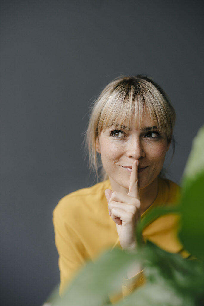 Stockfoto, lizenzfrei,vertikale Bilder, Stories, Storytelling, mobile-first,Porträt einer schönen blonden Frau, die lächelt und den Finger auf den Mund legt