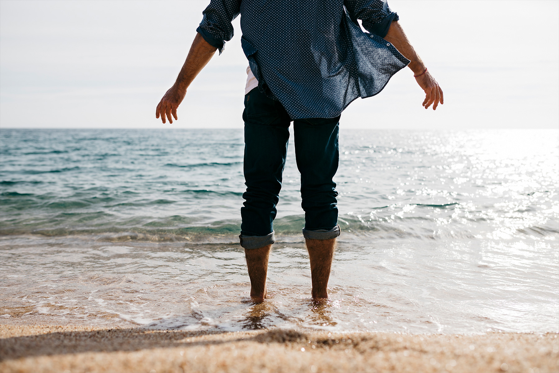 Stockfoto, lizenzfrei, Reifer Mann steht im Wasser Rand gegen klaren Himmel am Strand, Wasser, See, Sand, Hemd, Wind, Jeans