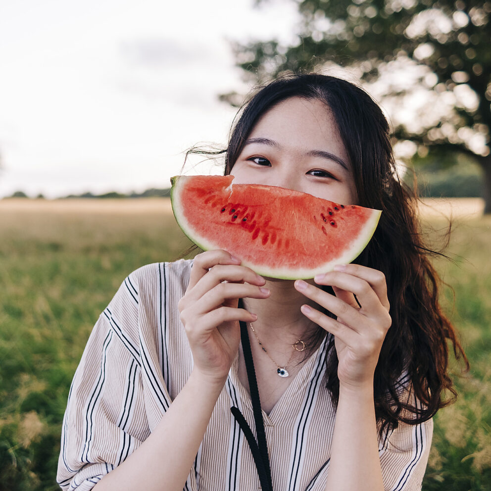 Stockfoto, lizenzfrei,Junge Frau bedeckt ihr Gesicht mit einer Wassermelonenscheibe auf einer Wiese