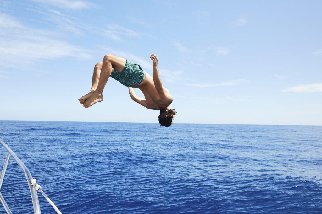 Stock image, royalty-free, Full length of man diving into sea against sky on sunny day, summer images, backflip, ocean, swimming, open water, boat