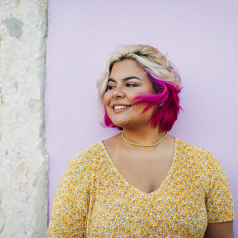 Lizenzfreies Stockfoto, Lächelnde Frau mit pinken Haaren, an der Wand stehend, Body Positivity