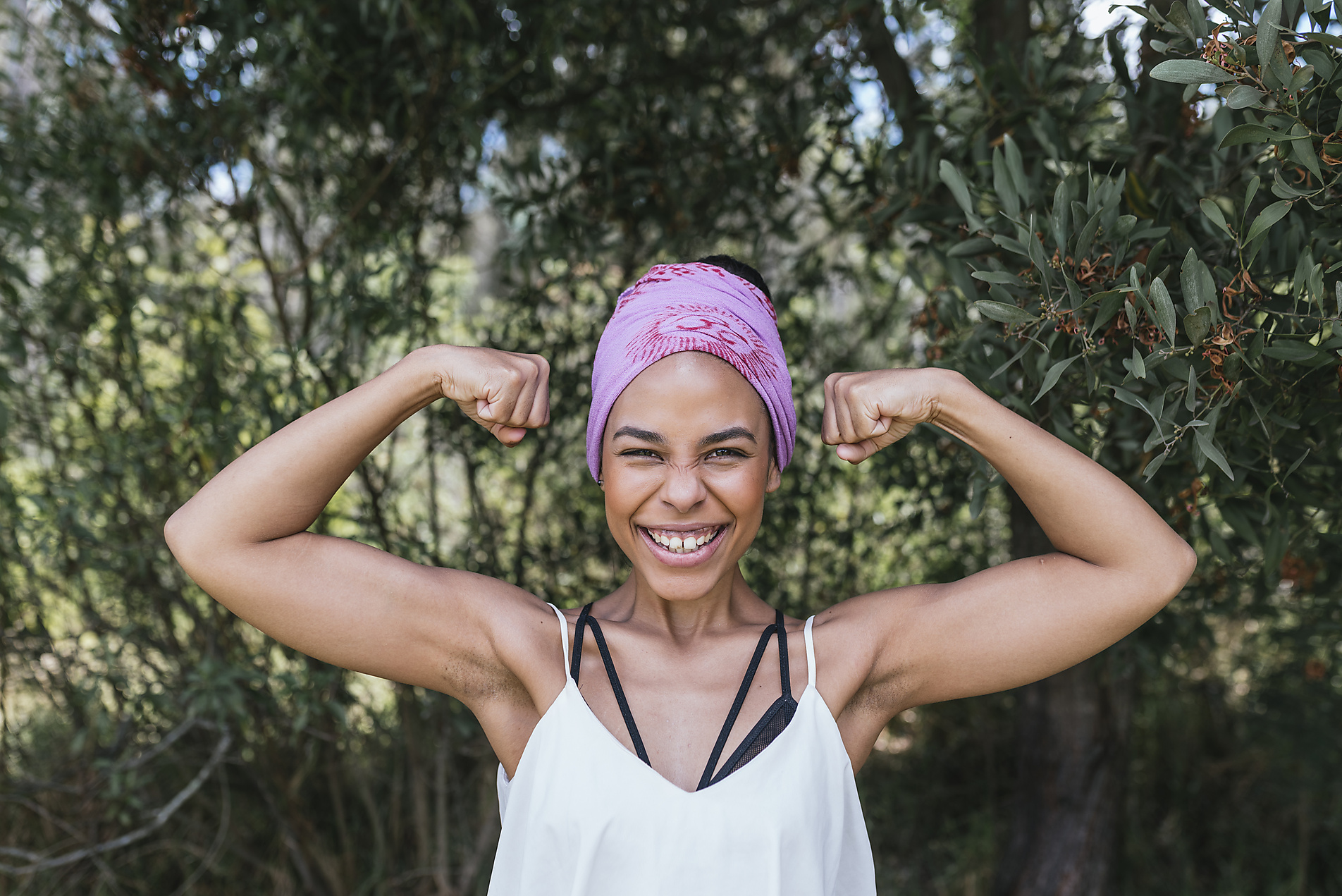 Stock image, royalty-free, Happy woman with purple bandana flexing muscles while standing against plants at park, summer, happiness,