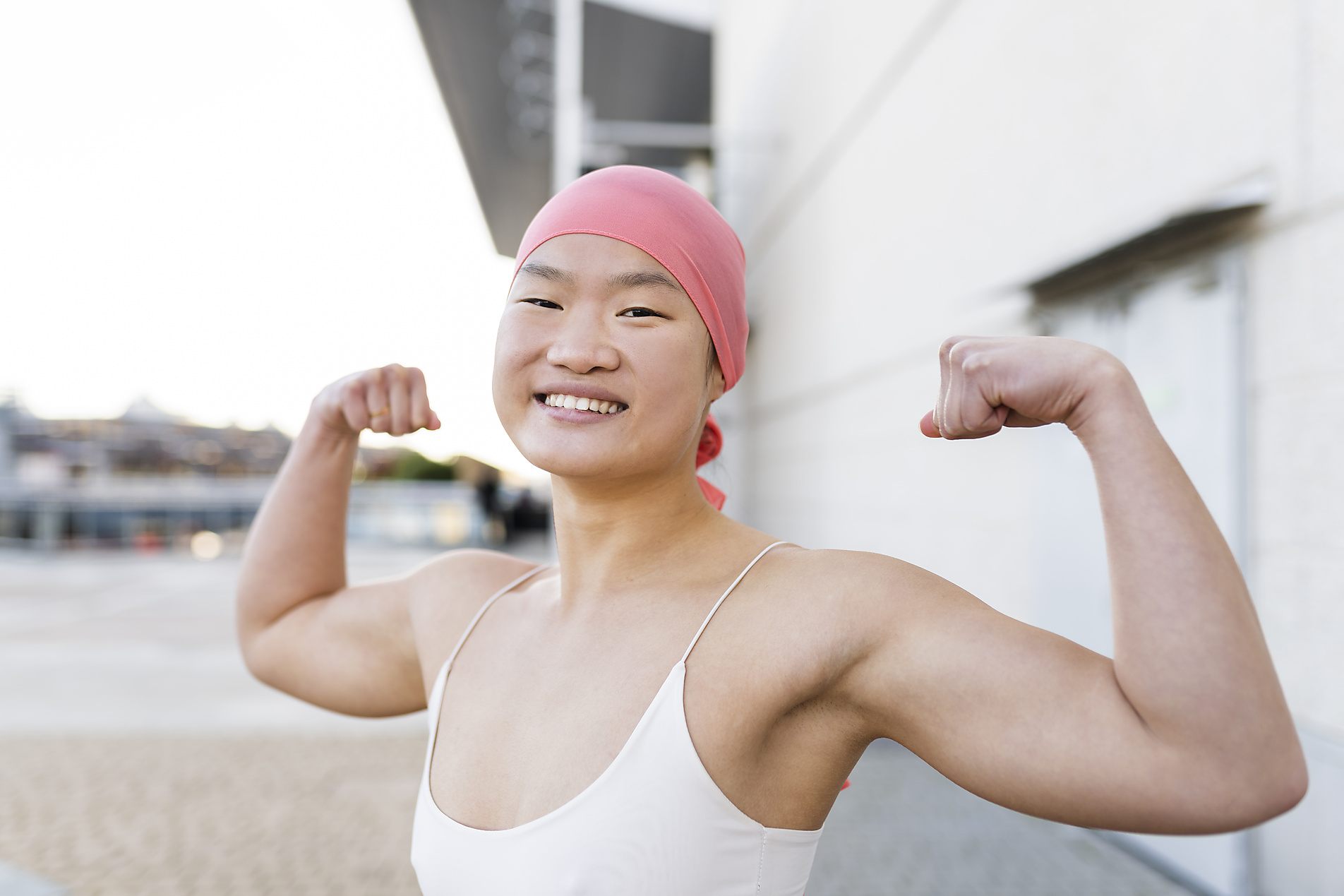 Stockfoto, lizenzfrei, Glückliche Frau mit rosa Kopftuch zeigt Bizeps, body positivity
