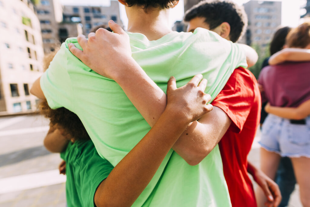 Stockfoto, lizenzfrei, multi-ethnische Freunde umarmen sich auf dem Fußweg stehend, Diversity, Sommer, Freundschaft, Frieden