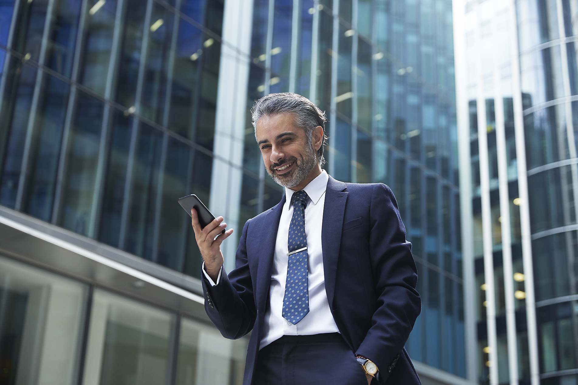 Stockfoto, lizenzfrei, Lächelnder Geschäftsmann benutzt Mobiltelefon vor einem Bürogebäude in der Stadt