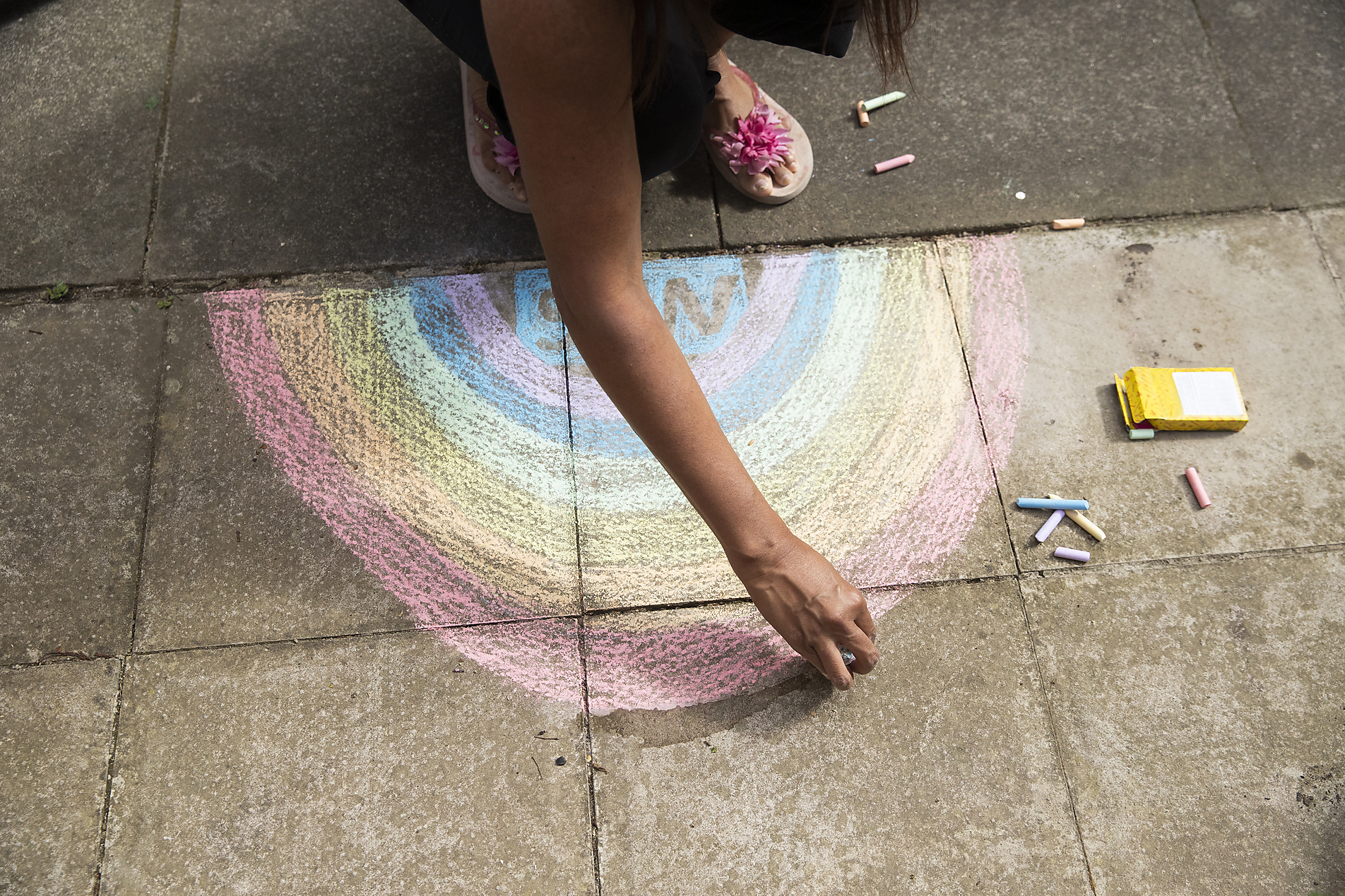 lizenzfreies Stockfoto, Arm einer erwachsenen Frau, die mit Buntstift einen Regenbogen auf dem Bürgersteig zeichnet
