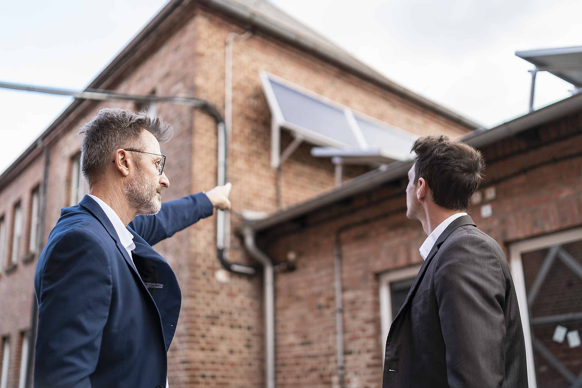 Stock photo, royalty free, businessman pointing to solar panels on a brick building, renewable energy, solar energy, energy transition, climate friendly, sustainable, environmental protection, climate neutral