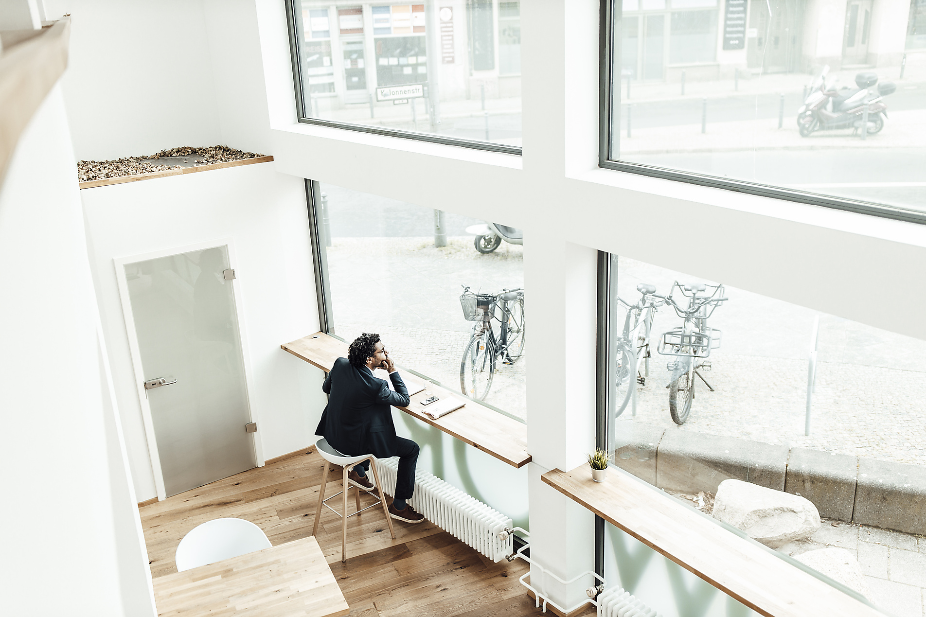 stock image, royalty-free, Thoughtful male entrepreneur sitting with hand on chin looking through window in office, homepage header