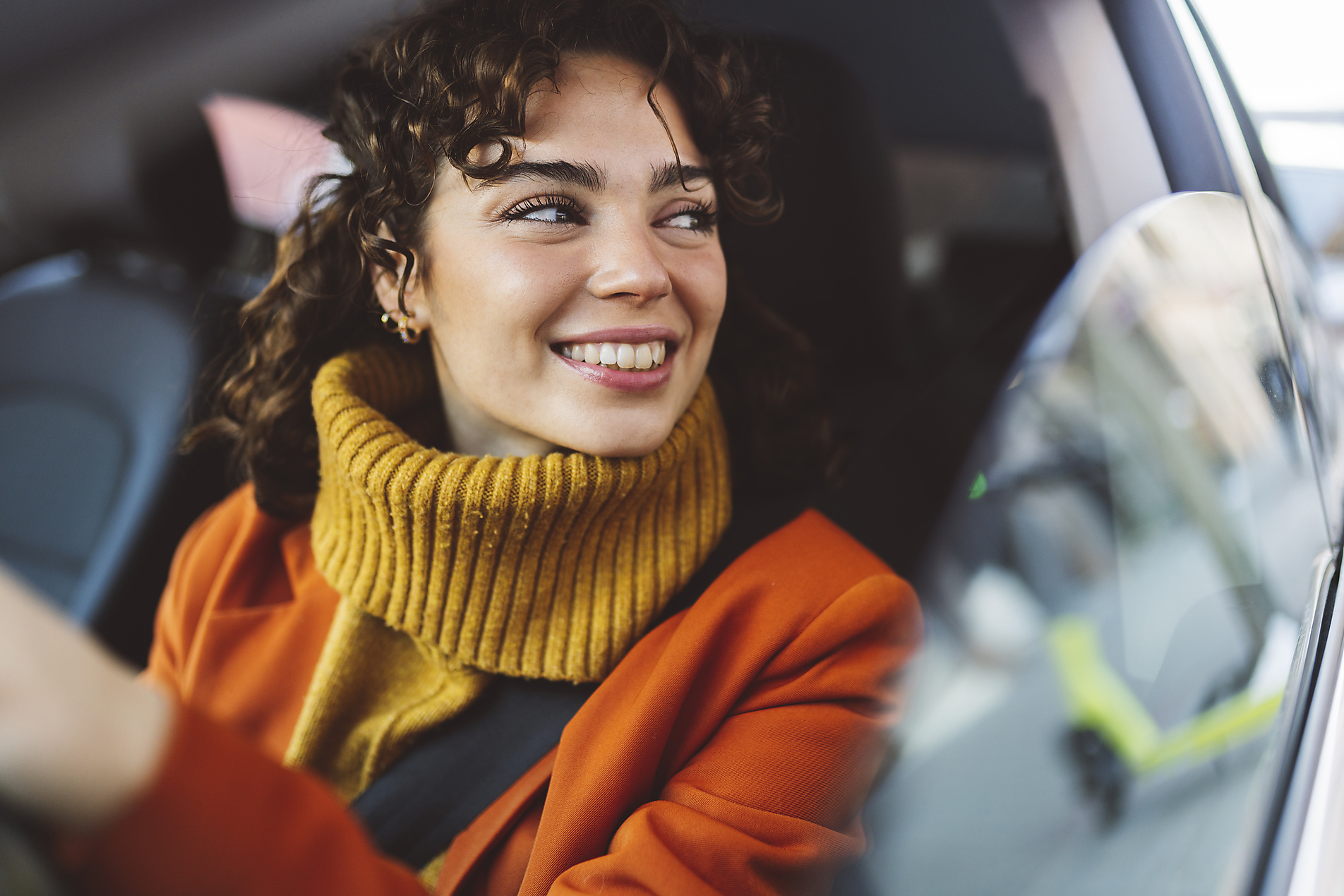Stock image, royalty-free, Smiling woman looking through window of car on road trip, city, yellow turtle neck, orange blazer