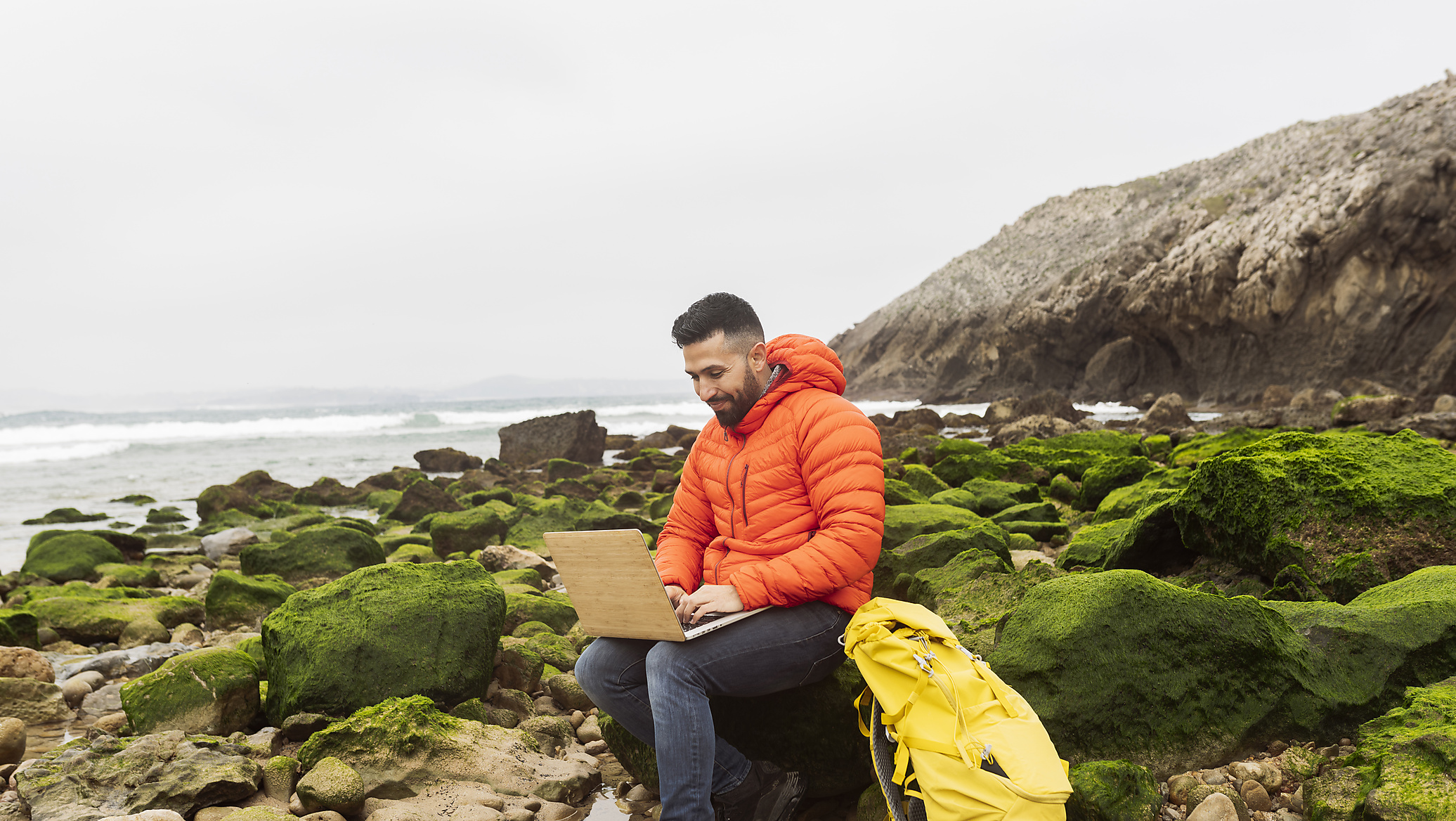 Stock image, royalty-free, Smiling man using laptop sitting with backpack on rock