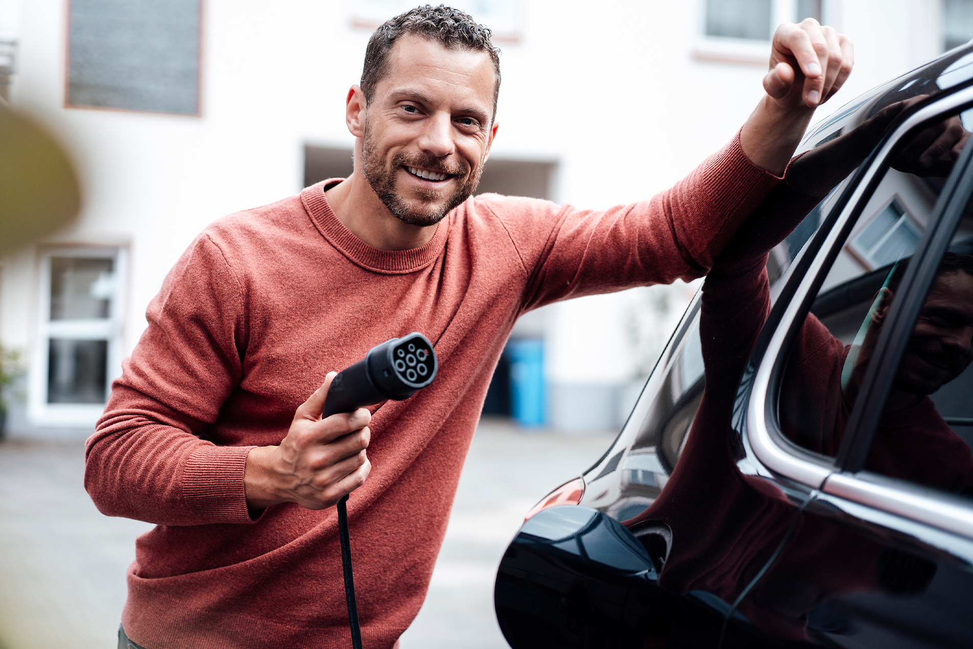 stock image, royalty-free, Smiling man holding charging cable leaning on electric car