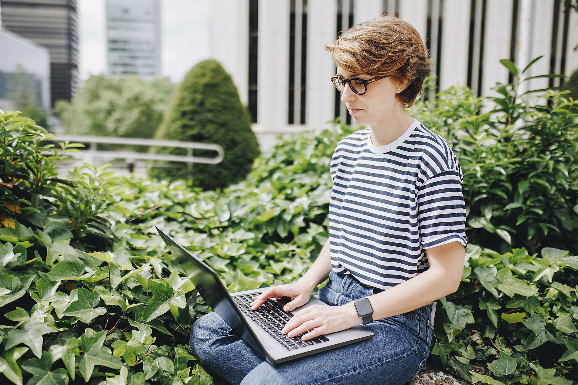Stock image, royalty-free, Woman working on laptop sitting amidst plants