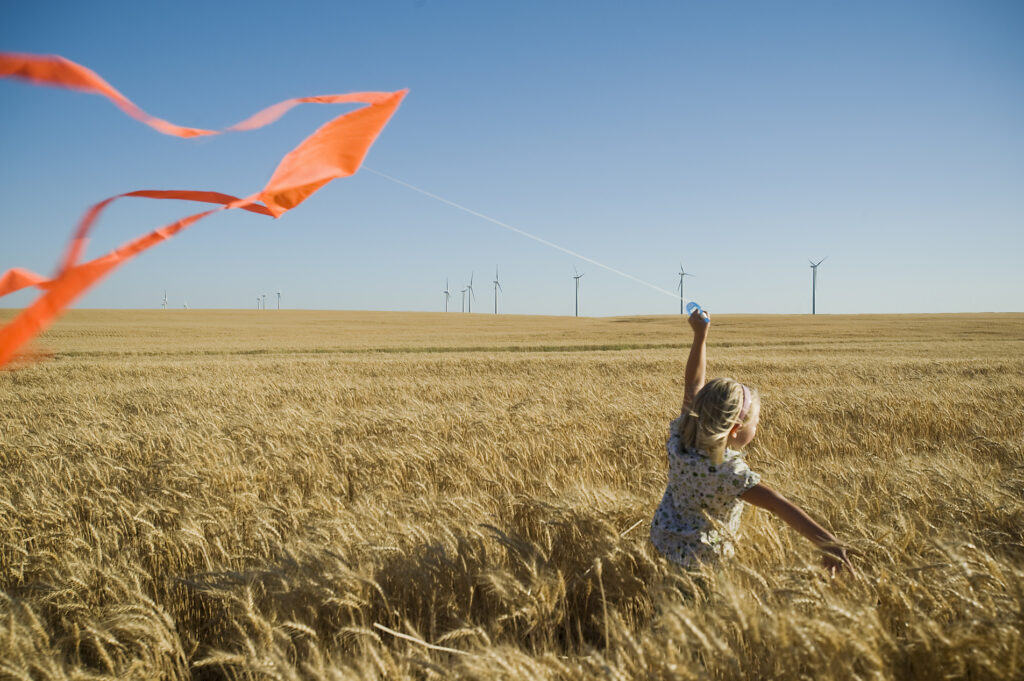 girl running through a field holding a kite, windpark, windmills, renewable energy, energy turnaround, climate change