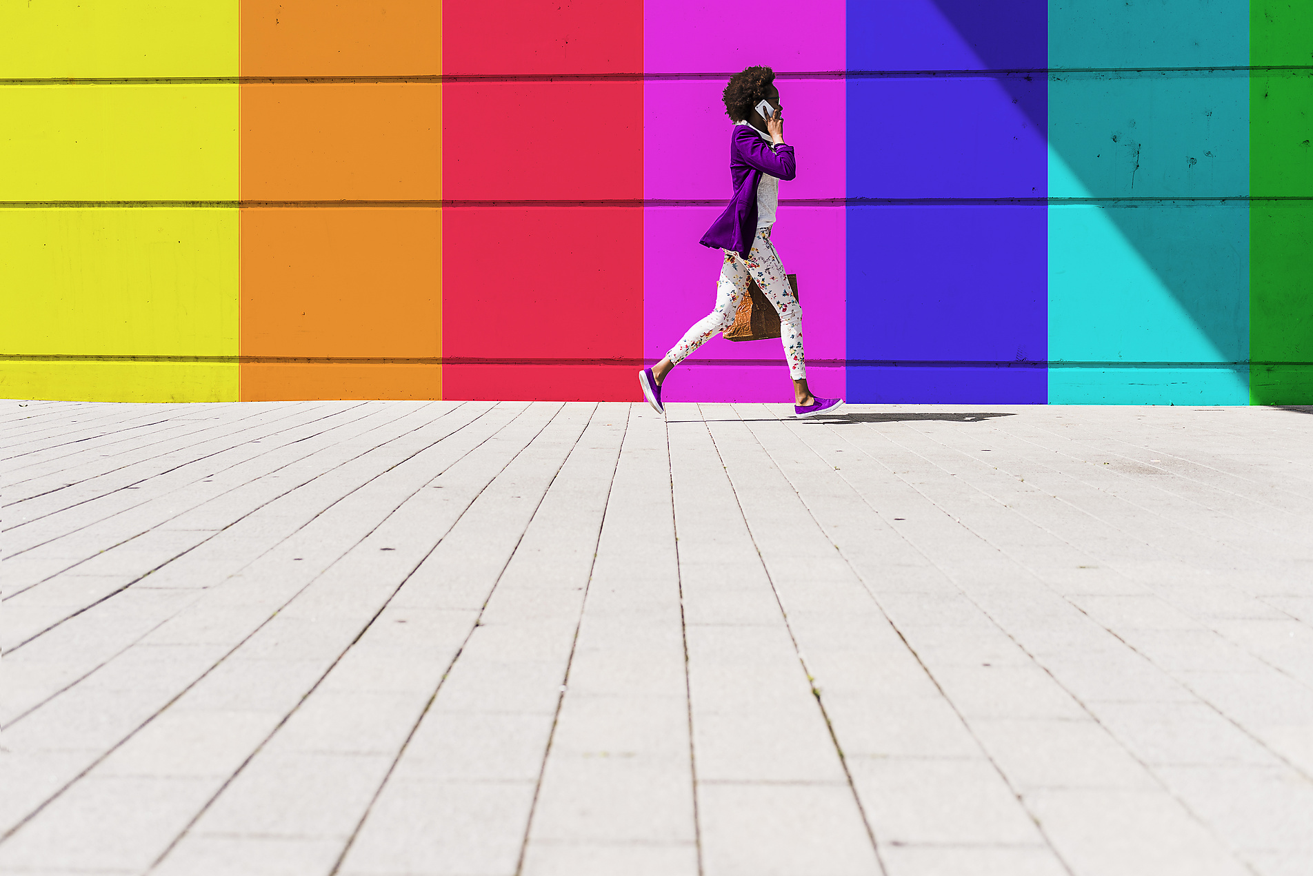 stock image, royalty-free, Young woman talking on smart phone while walking by colorful wall during sunny day, homepage header