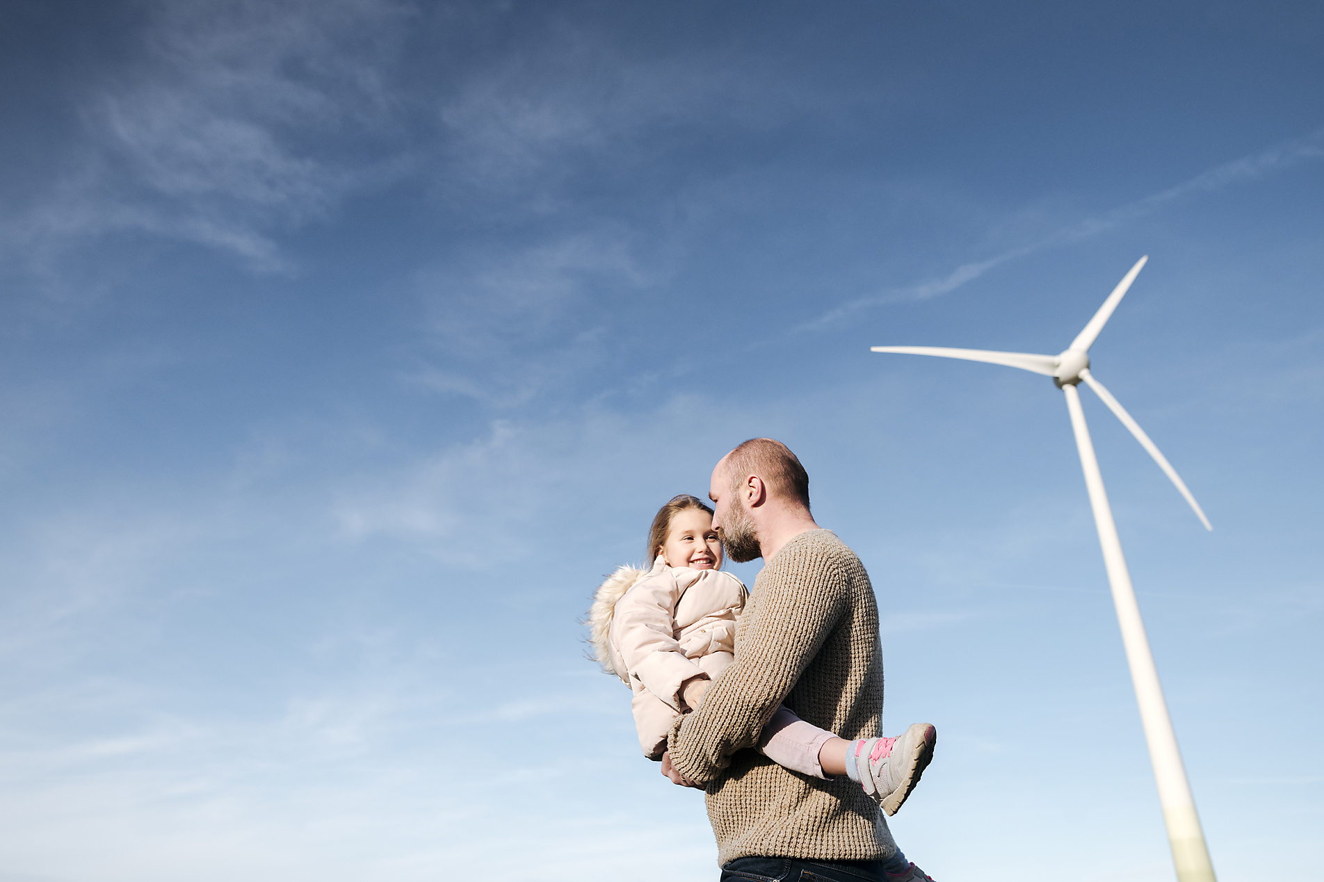 Stock image, royalty-free, Father holding his daughter in front of a wind turbine, energy transition, climate change, sustainable, emission free, climate positive, wind energy