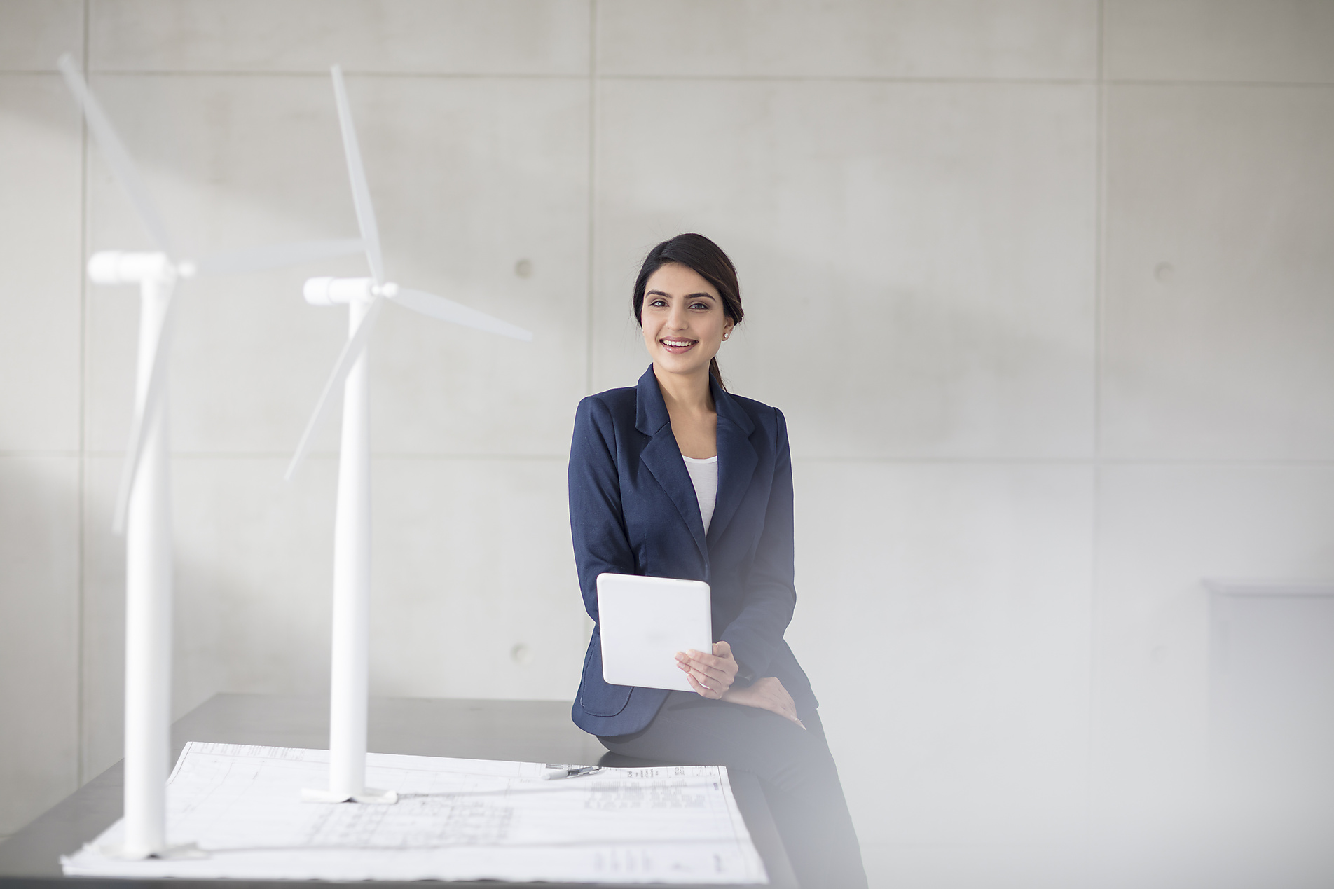 stock image, royalty-free, Portrait of smiling young woman with wind turbine models and tablet in office, wind energy, sustainable, emission-free, climate positive,
