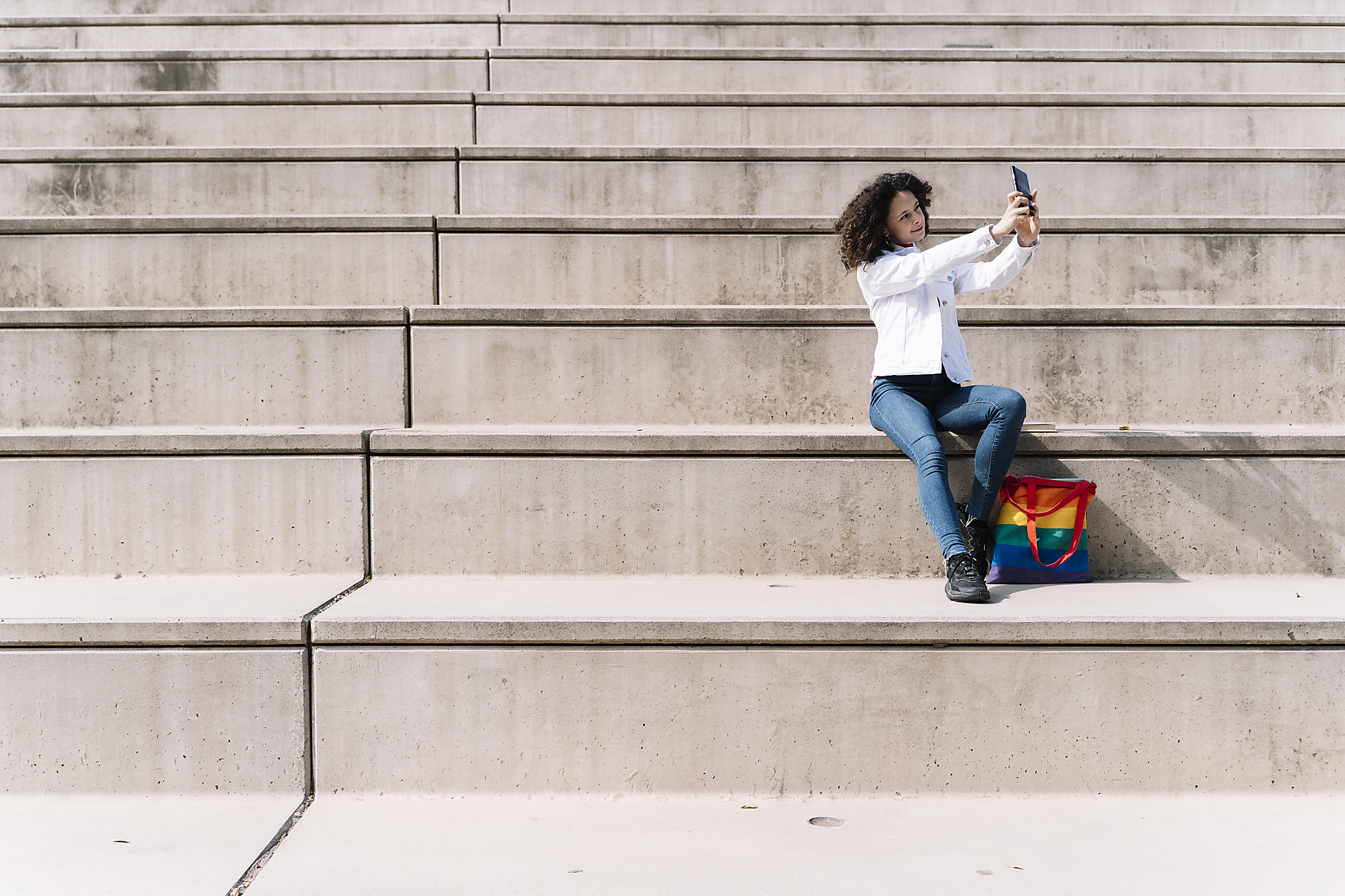 Stock image, royalty-free, Hispanic woman taking selfie on smart phone while sitting on steps during sunny day